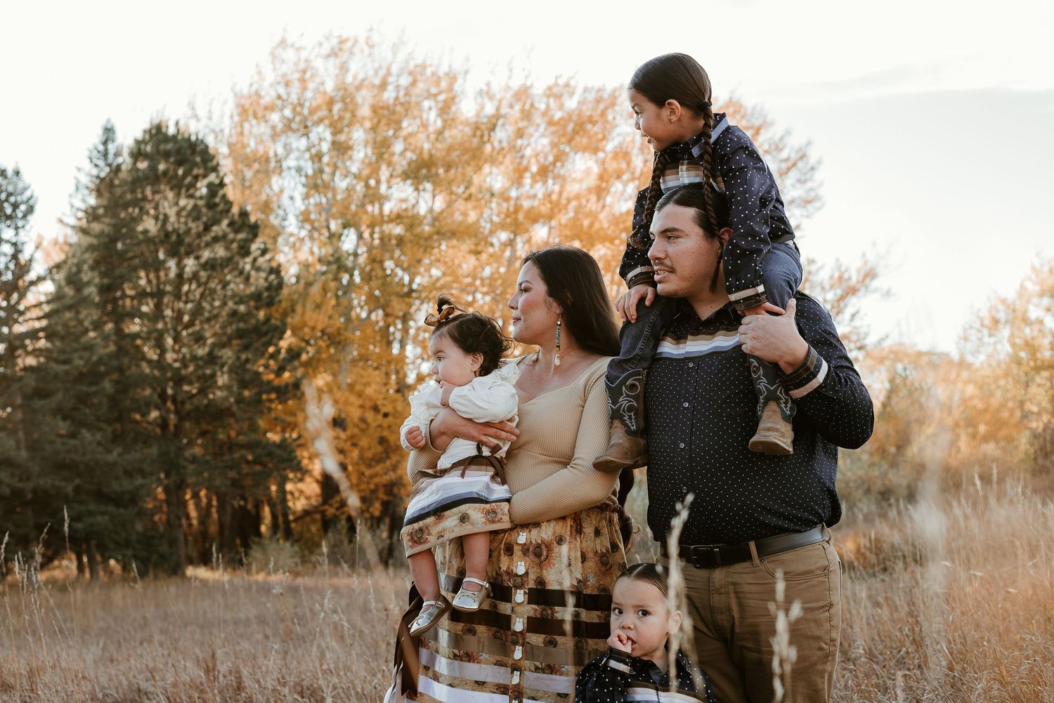 Candid family portrait in a rustic field during golden hour with fall foliage in background.