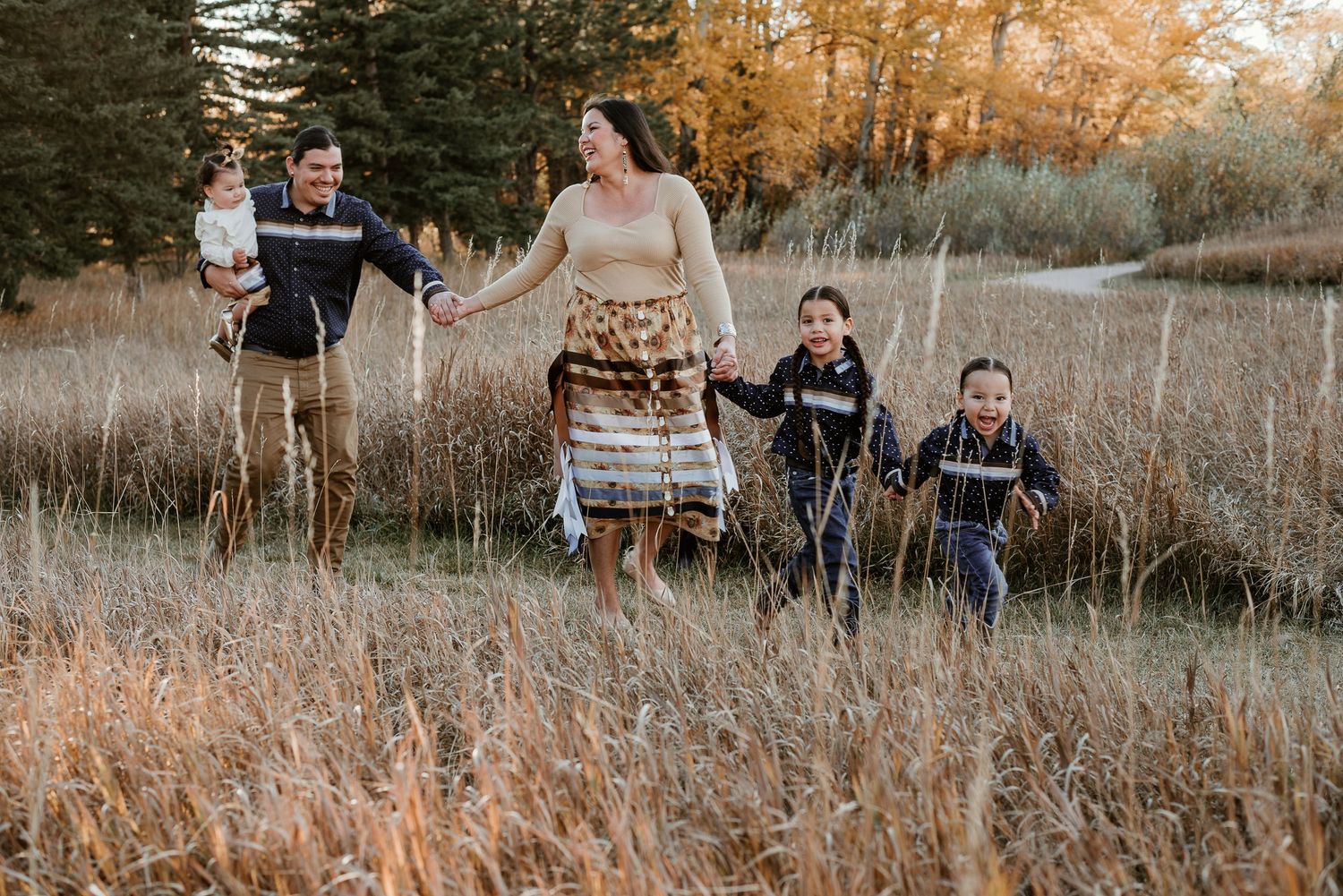 Family walking through tall grass with mountains and trees in background.