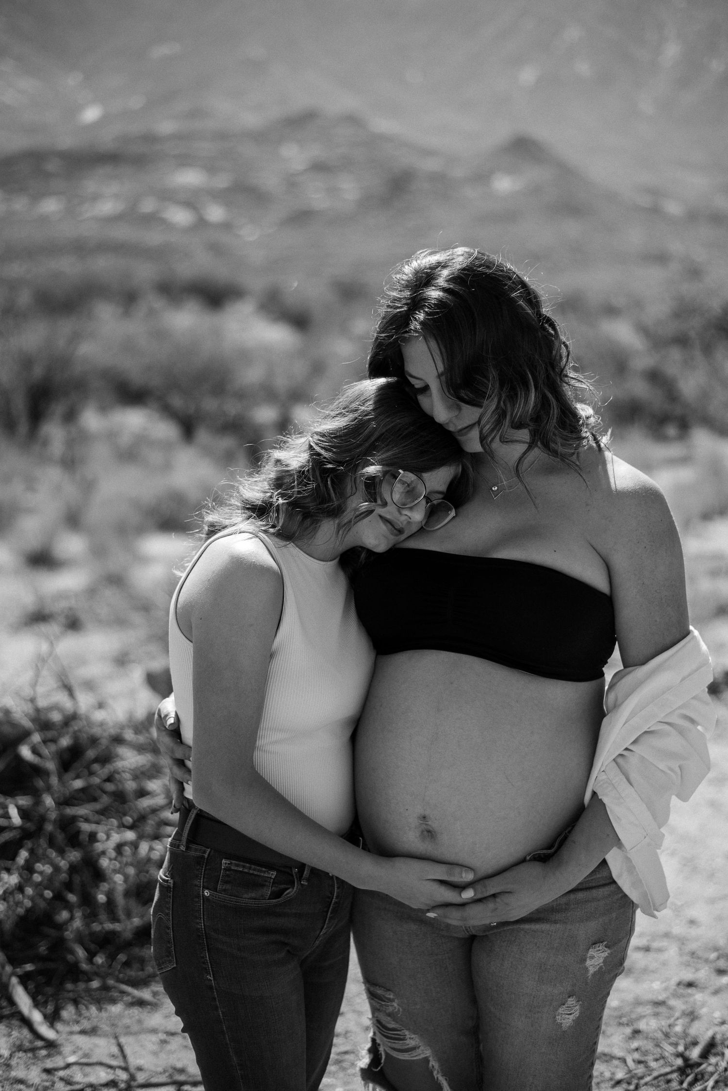 Black and white photo of people embracing against a desert mountain backdrop.