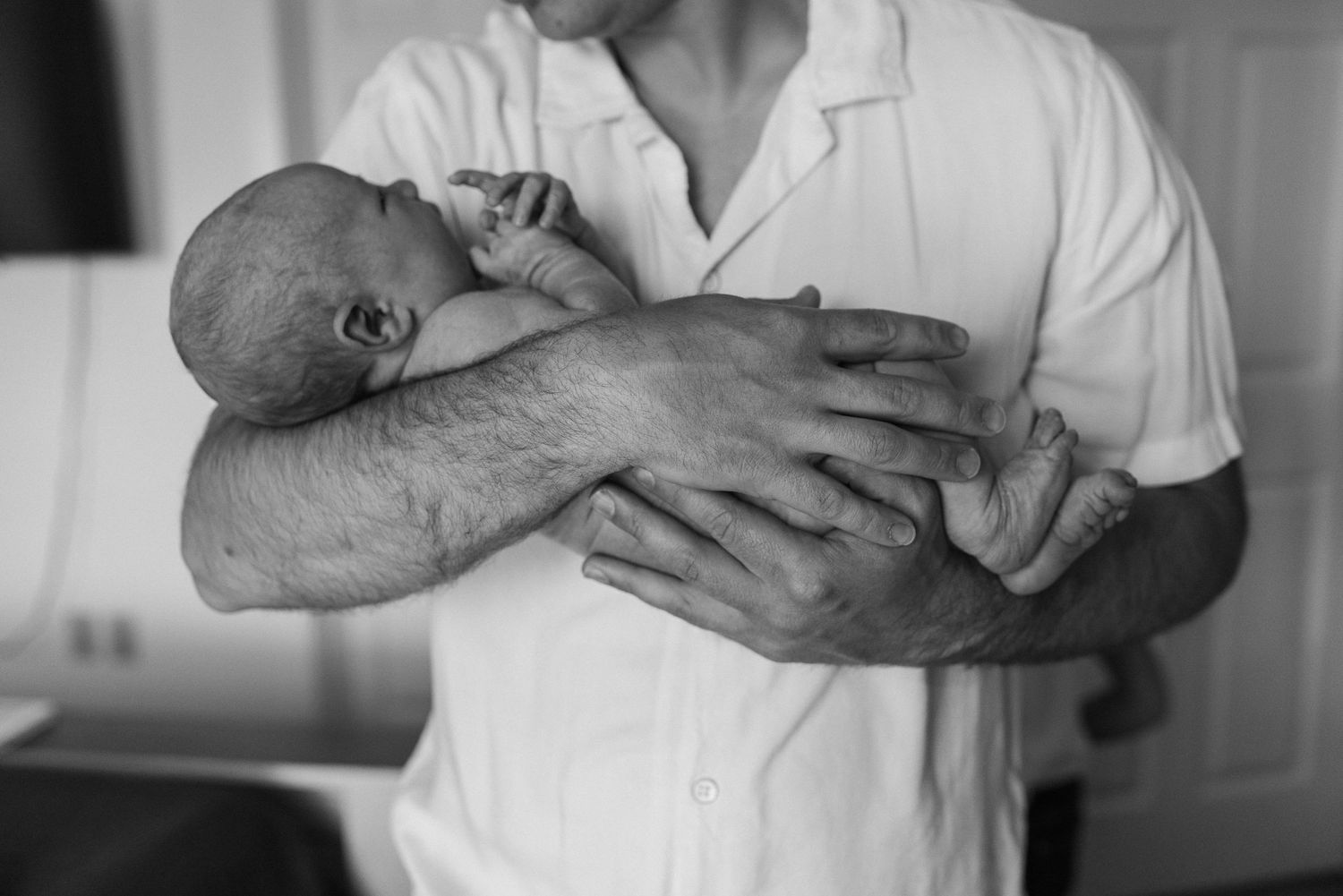 A tender black and white portrait of a newborn being cradled.