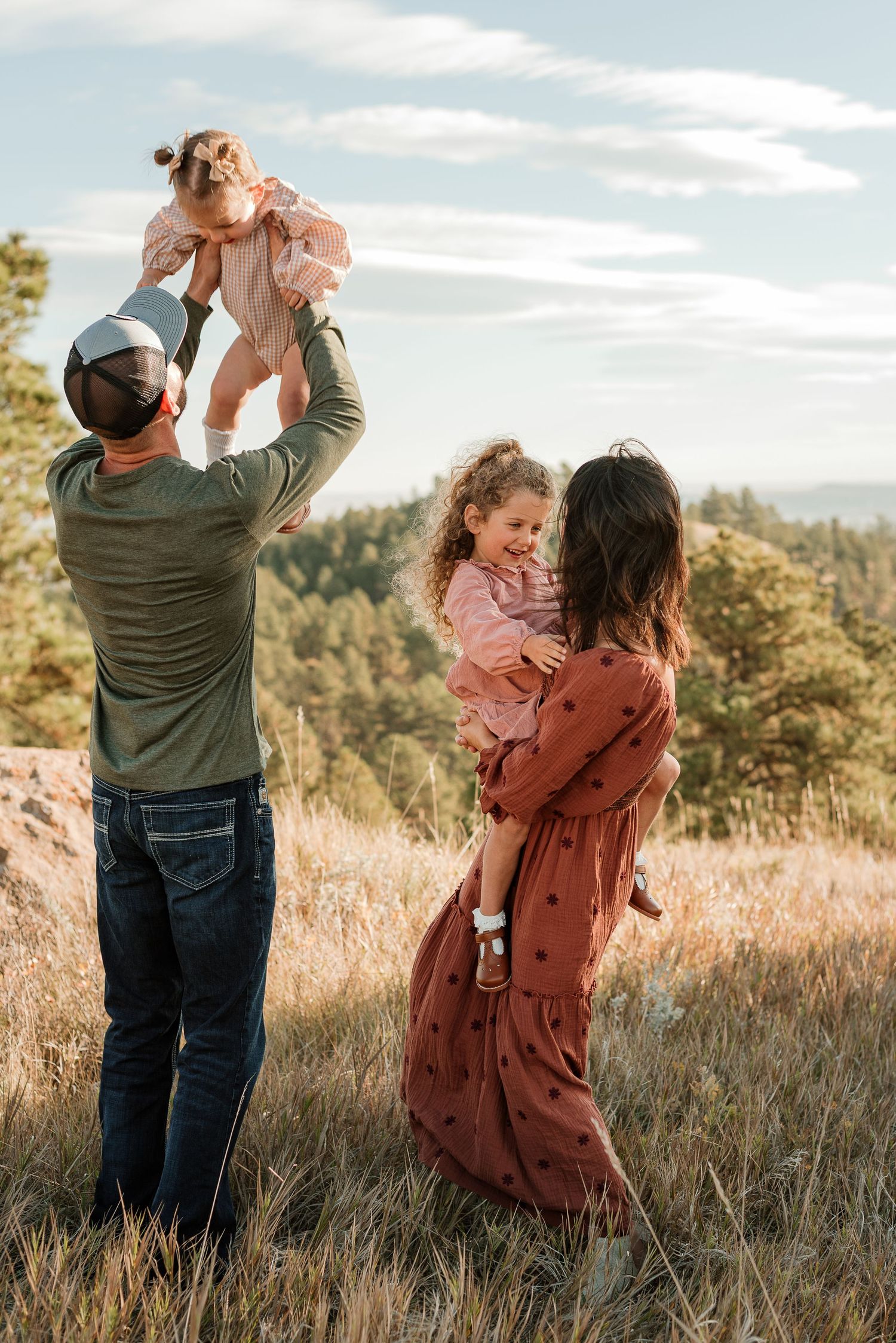 A family shares tender moments together in a golden field at sunset as they embrace and play with their child.