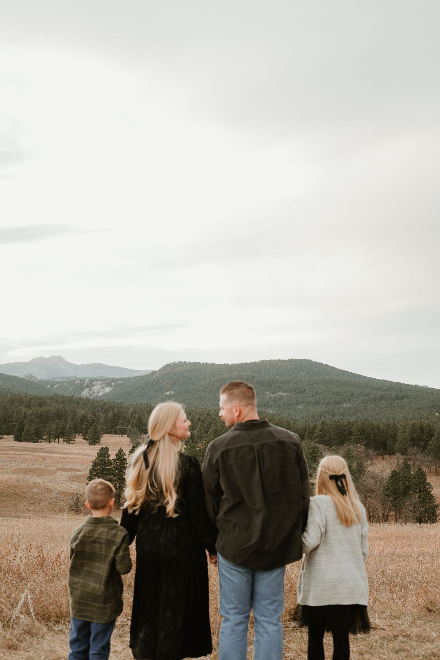 A family admires the mountain vista together while standing in a golden field on an overcast day.