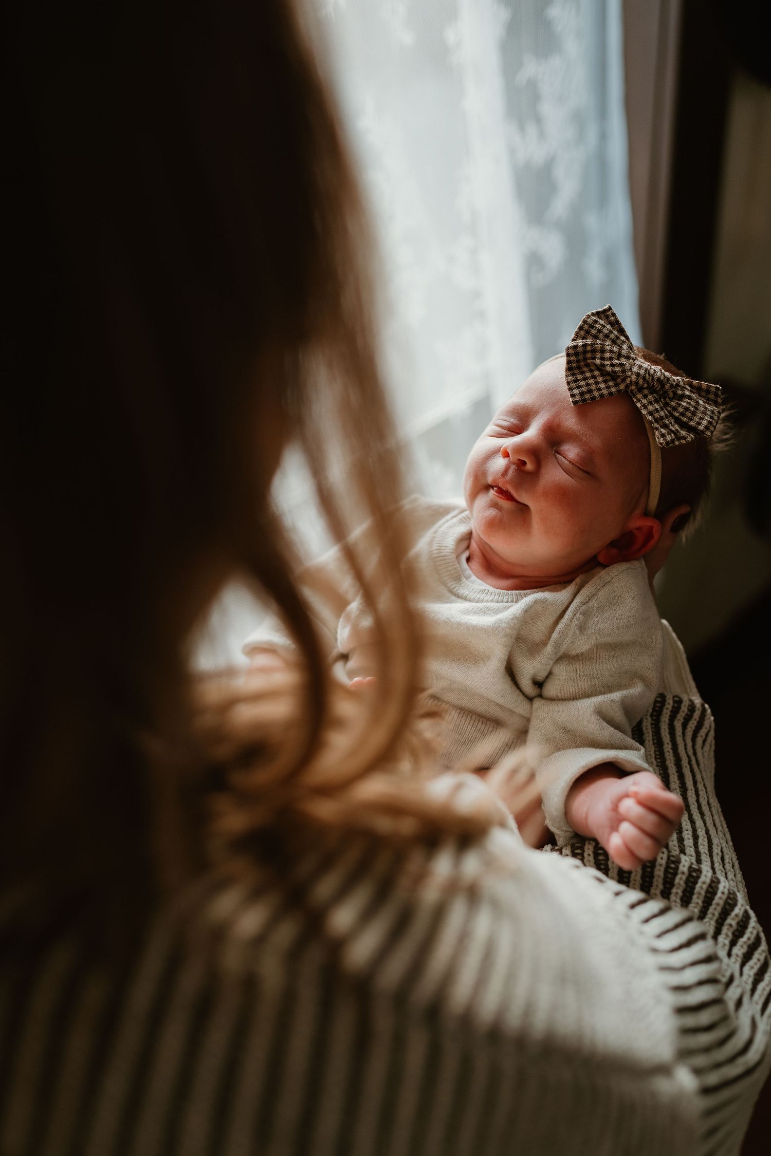 A sleeping newborn wearing a bow headband photographed in soft natural window light.