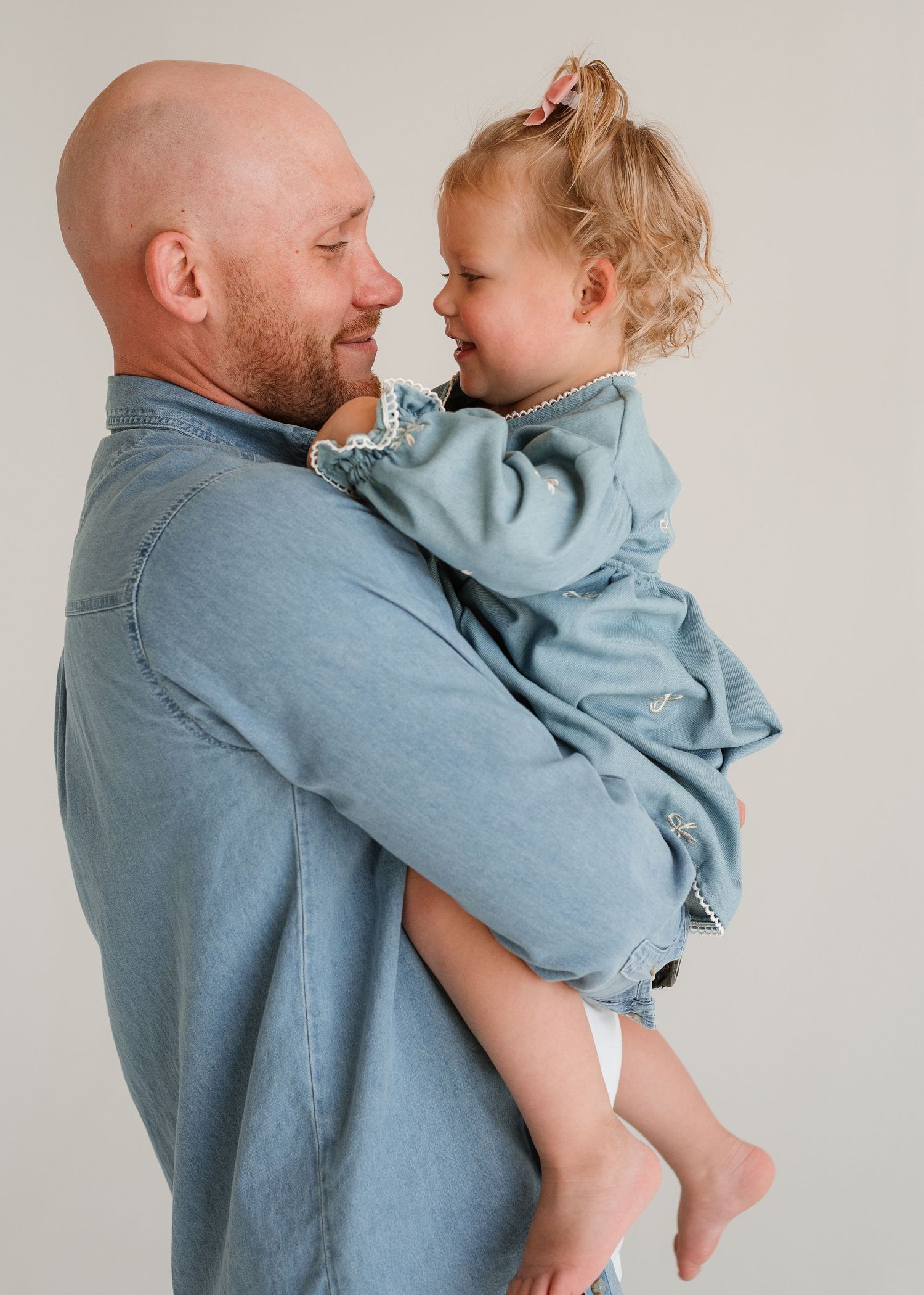 Parent in denim shirt holds and interacts with small child wearing light blue outfit in progressive side view sequence.