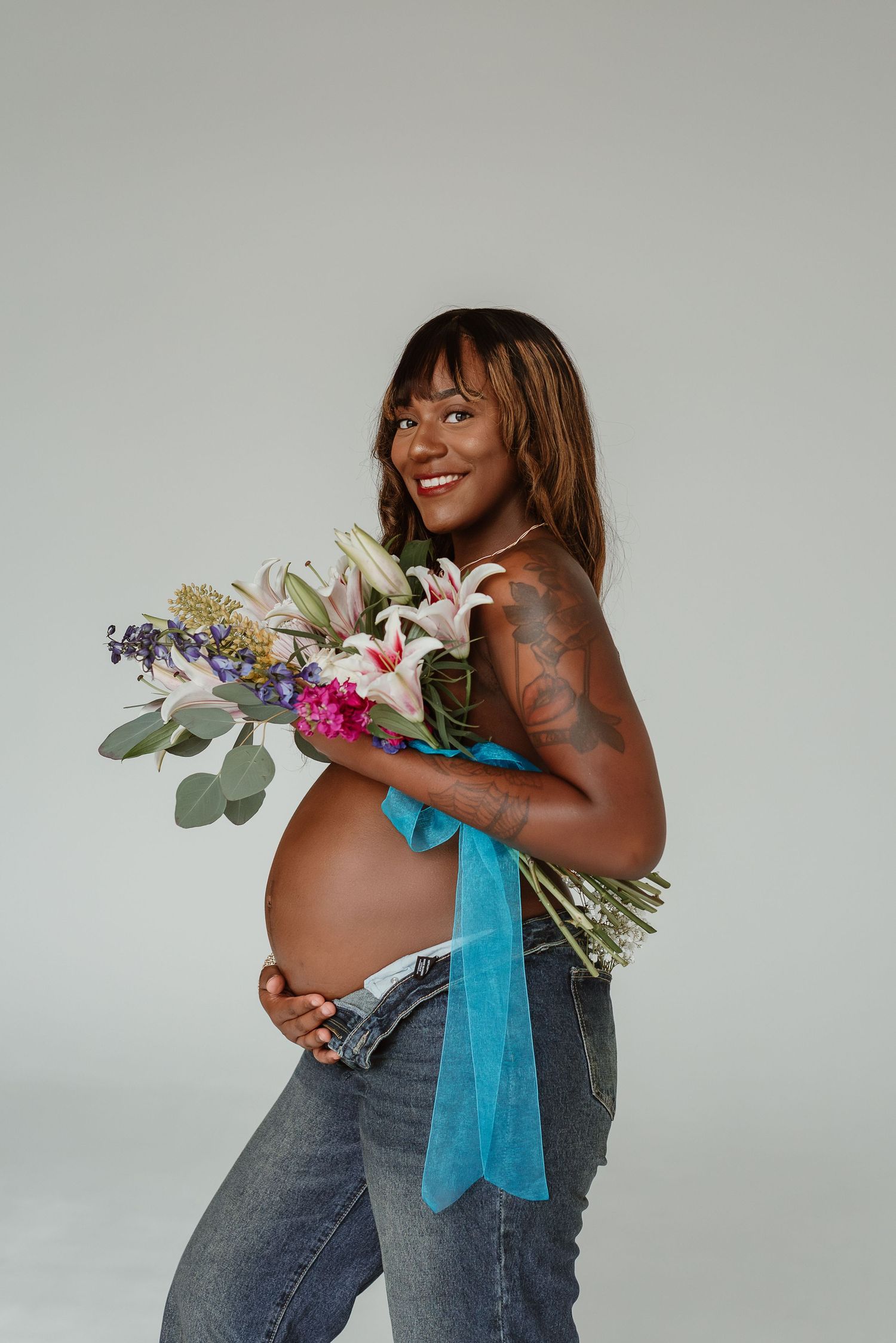 A series of maternity photos showing a pregnant figure in jeans holding colorful floral arrangements with a blue ribbon.
