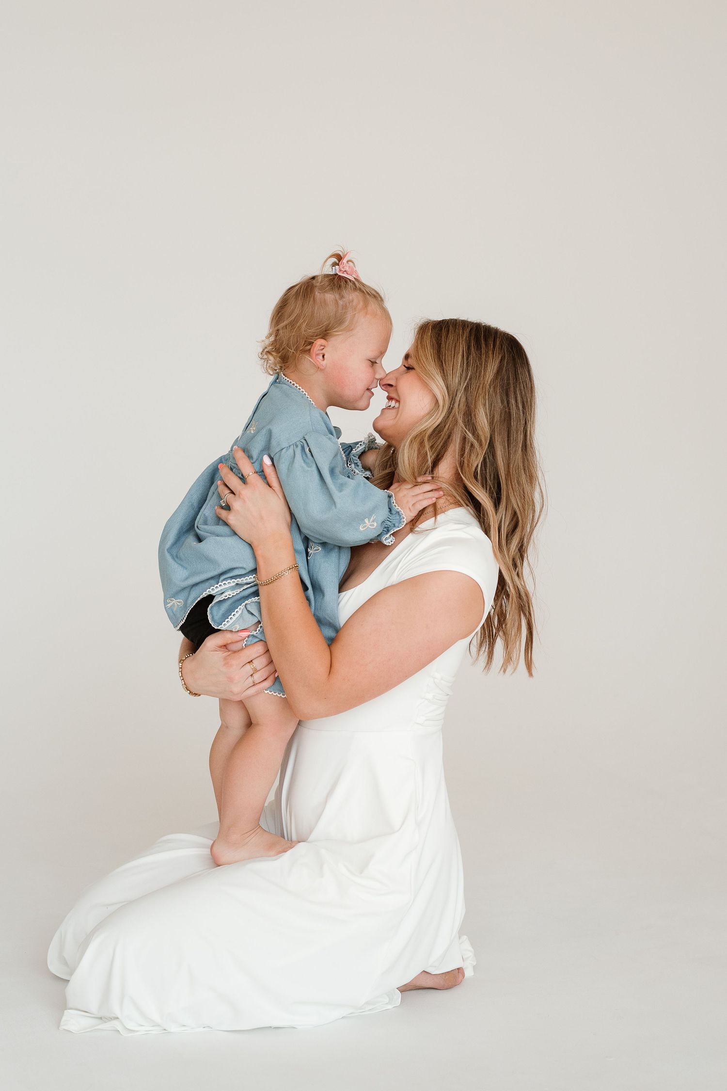 A tender moment between parent and child wearing white and blue against a light gray studio backdrop.