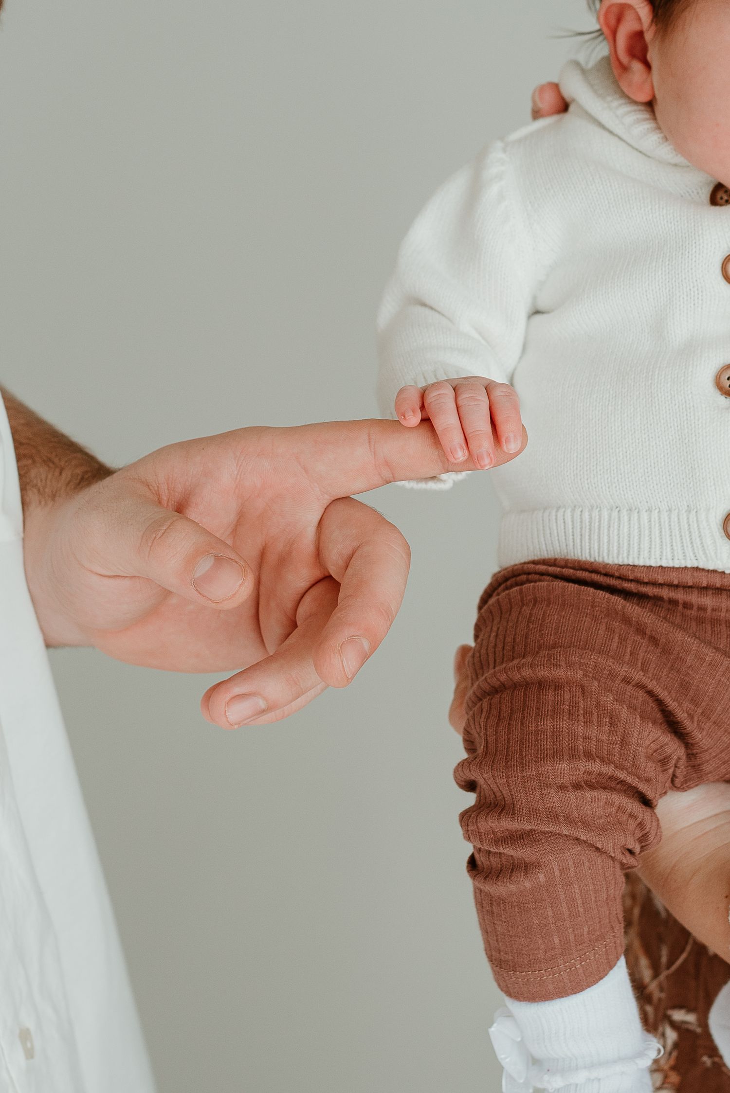 Close-up view of baby's hand reaching up while wearing white and brown clothing.