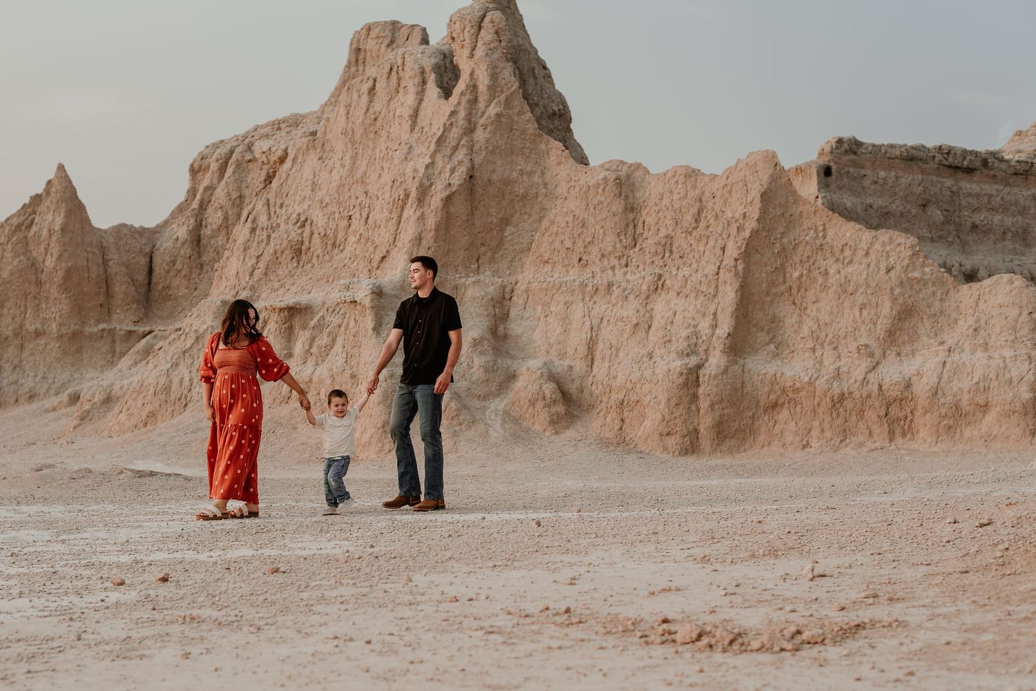 Group walking along a wooden pathway through dramatic desert rock formations.
