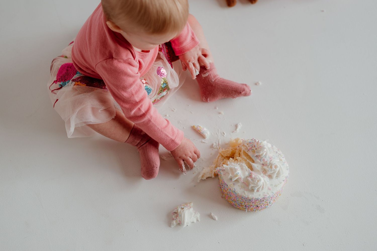 A baby in pink pajamas plays with shredded paper on the floor, making a playful mess.