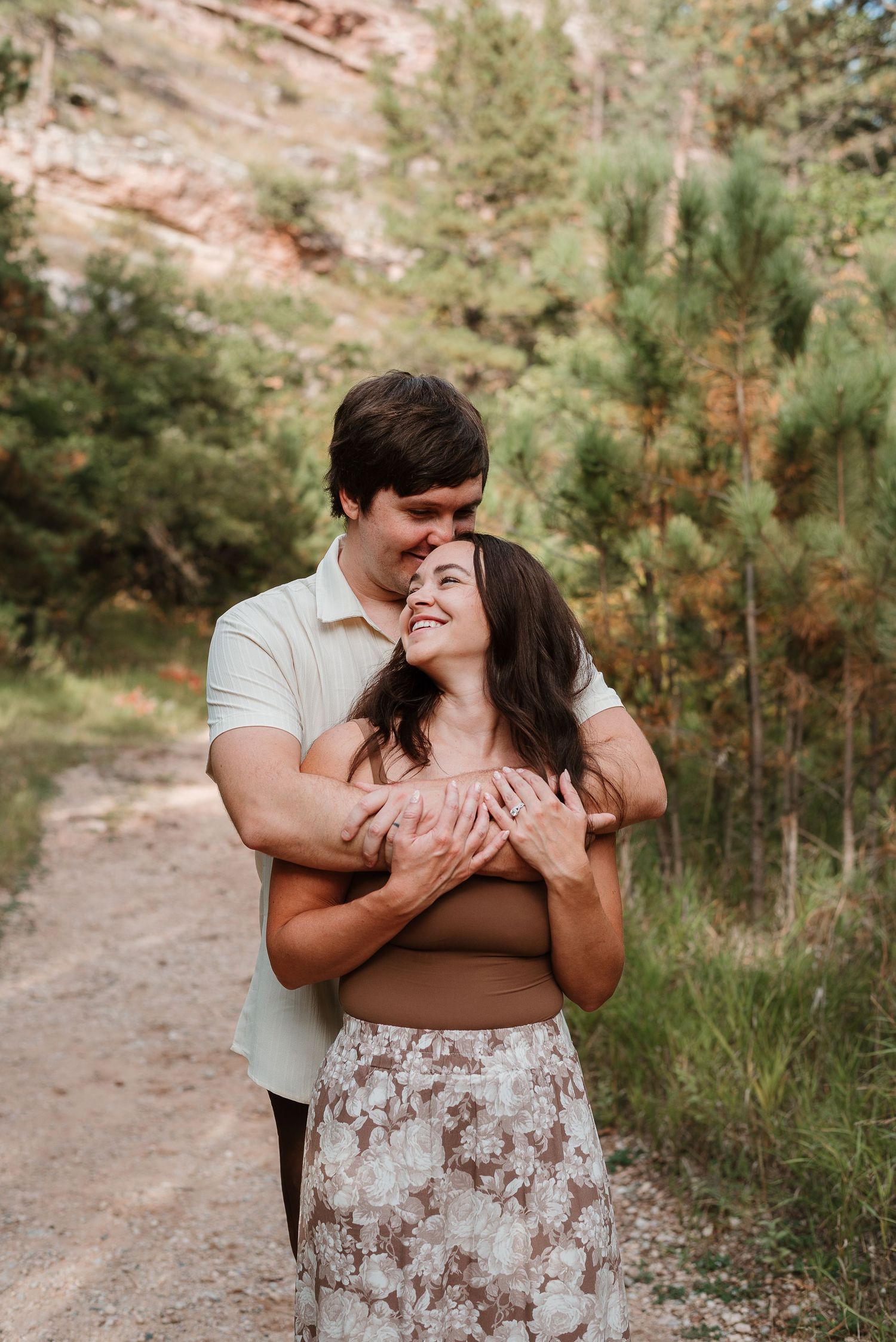 A romantic outdoor photoshoot in a wooded area with a couple embracing on a dirt path.