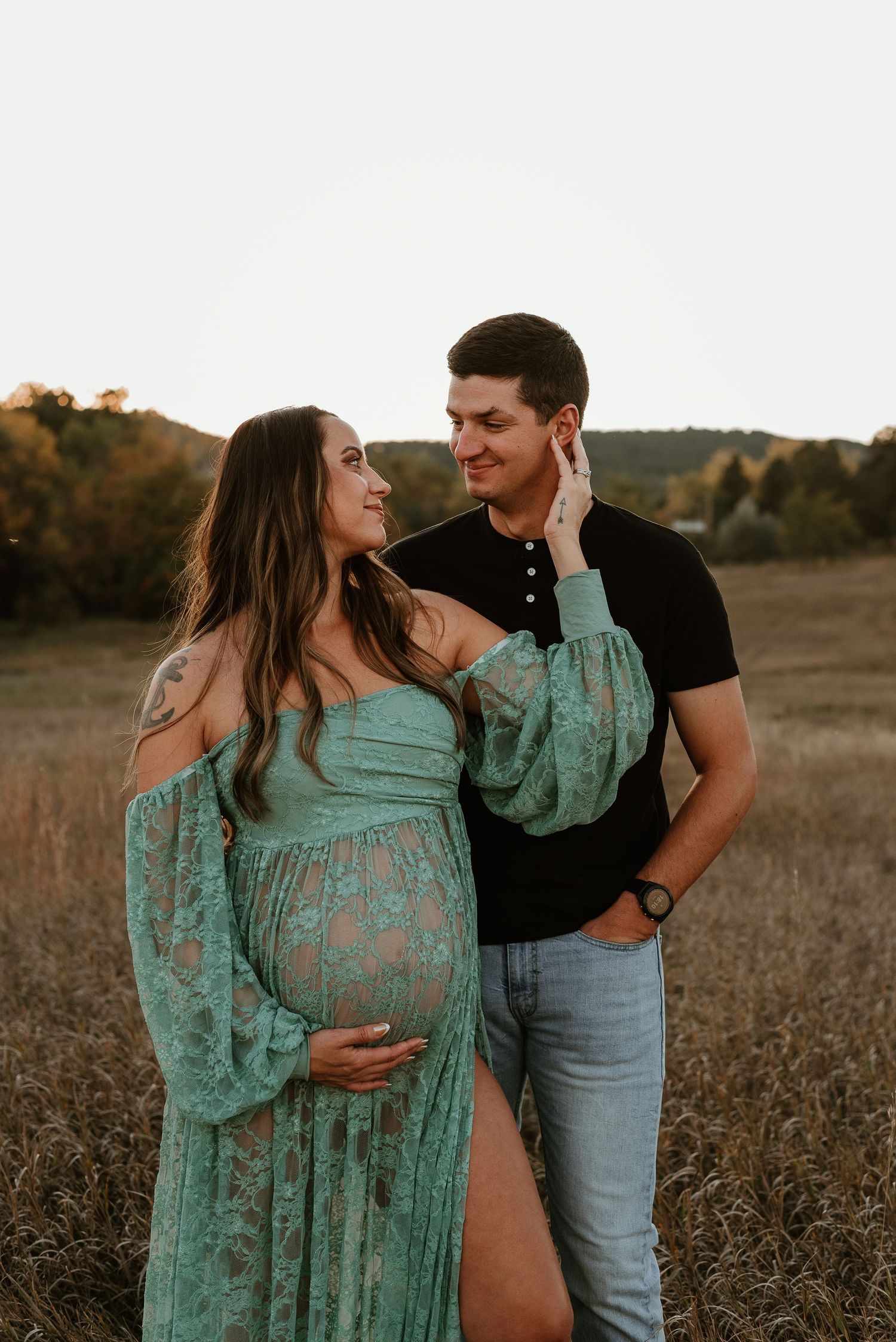 Romantic maternity photo session in a field at sunset showing couple in casual attire and mint green dress.