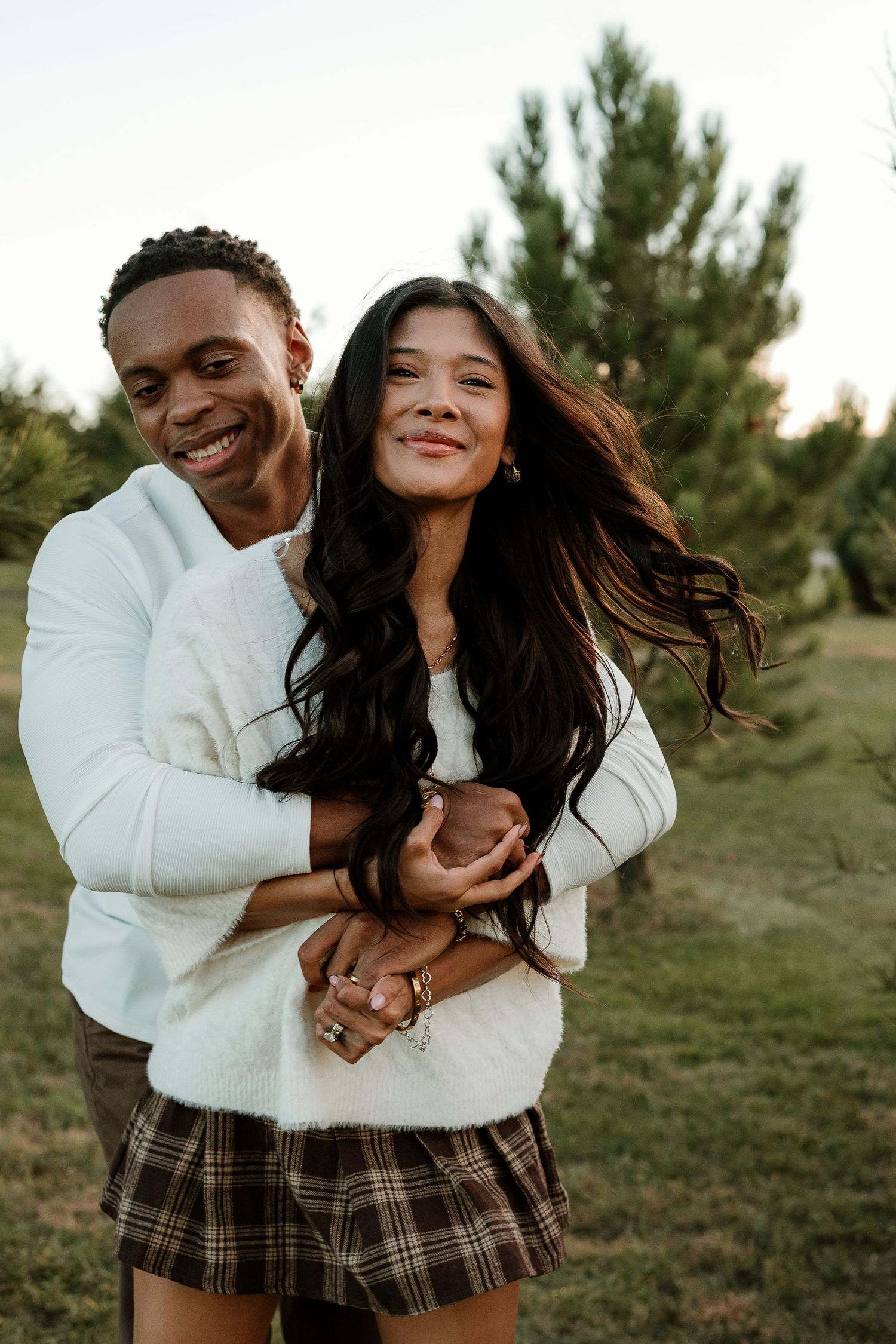 Joyful couple laughing and embracing in coordinated outfits during outdoor photoshoot.