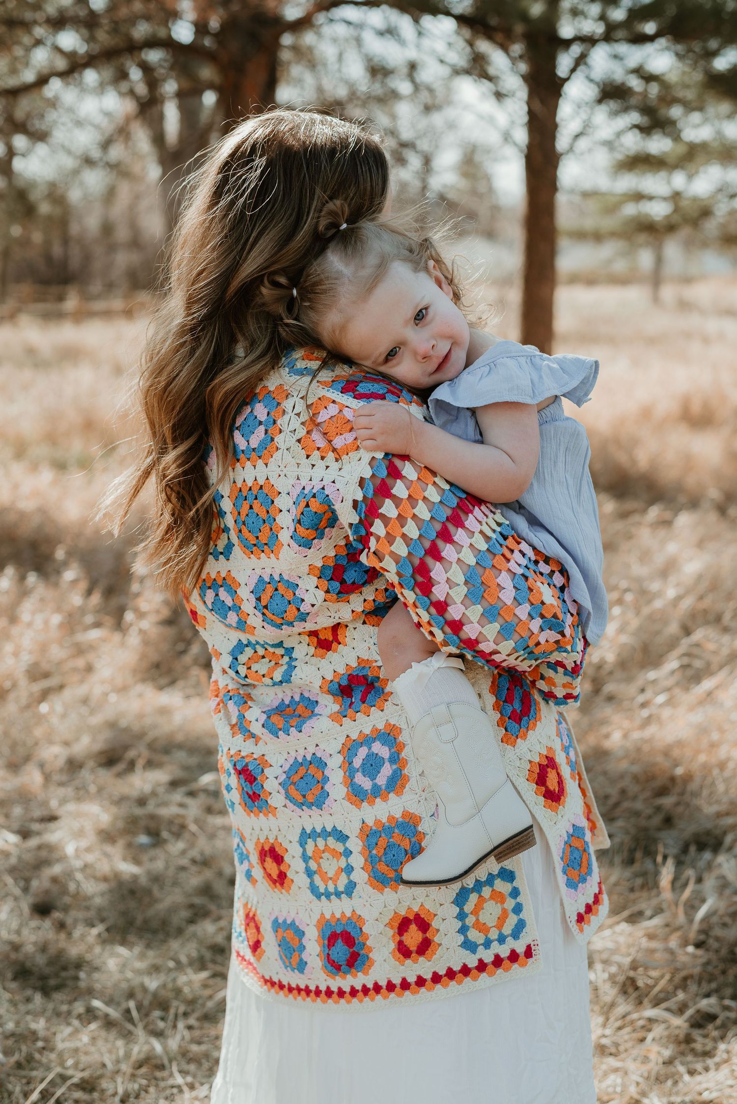 A colorful crocheted granny square cardigan is worn in an outdoor photoshoot against a natural backdrop.