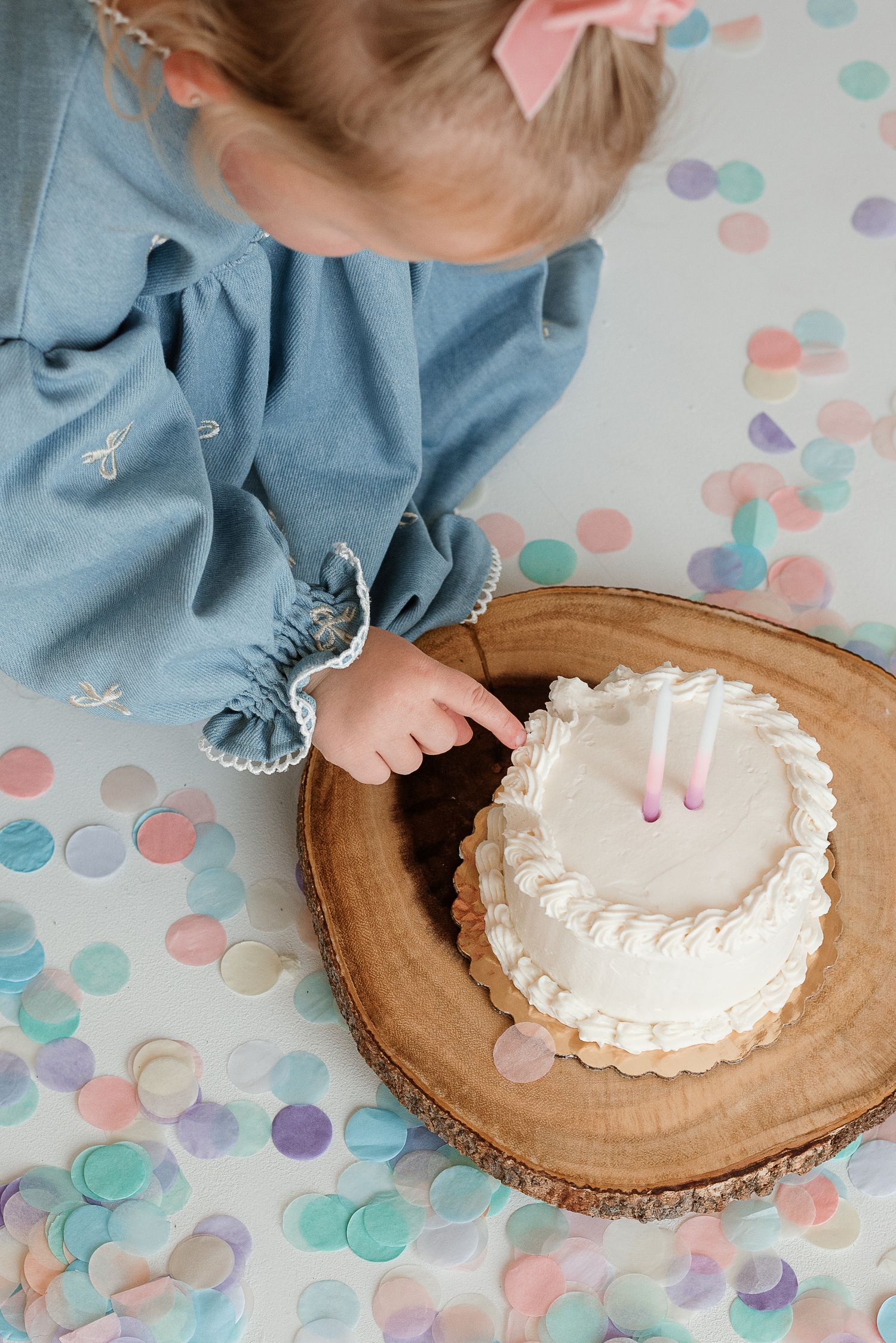 A small white smash cake sits on a wooden slice with pastel polka dot background.
