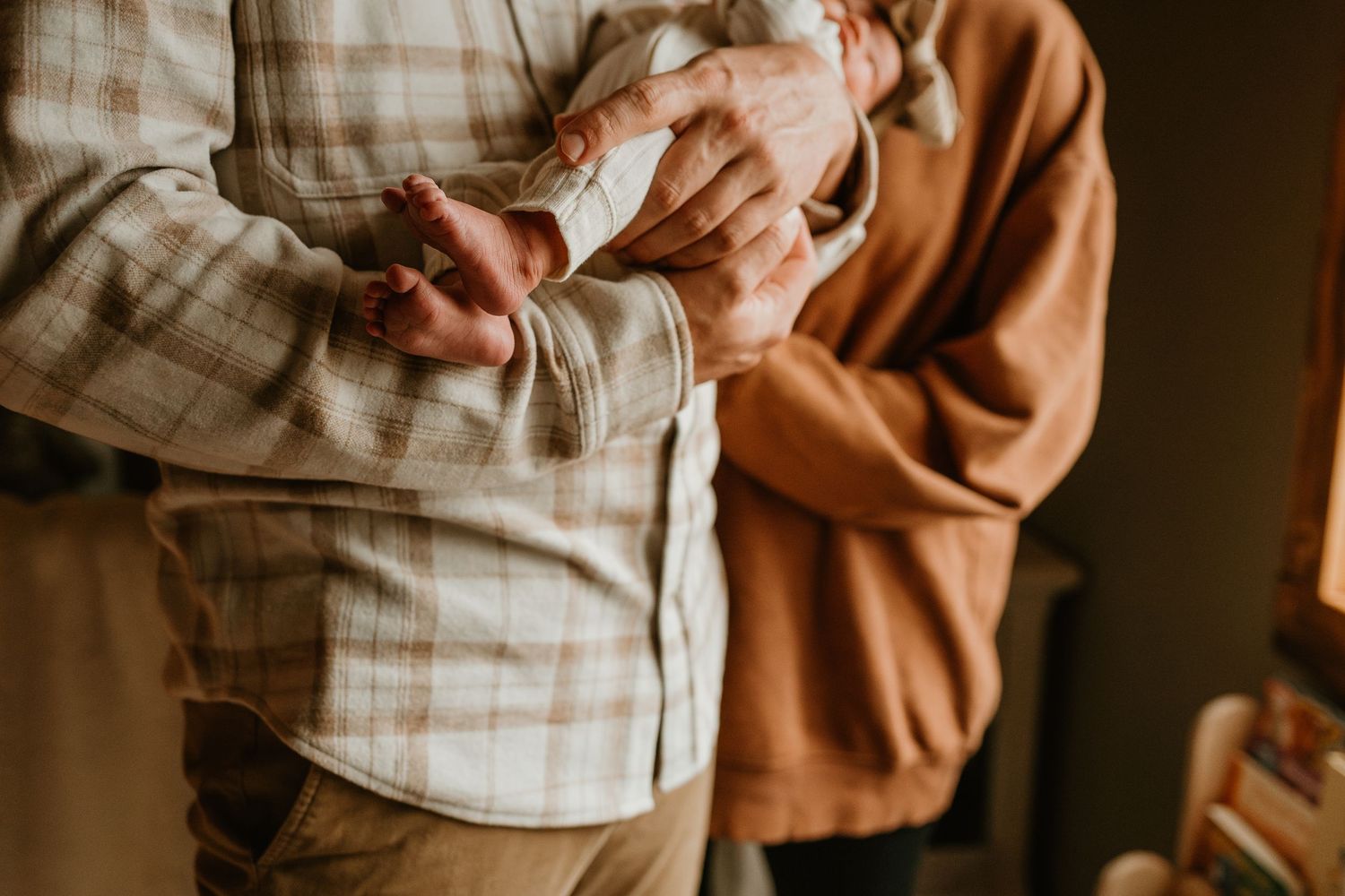 A tender moment between a parent and newborn baby swaddled in a brown blanket.