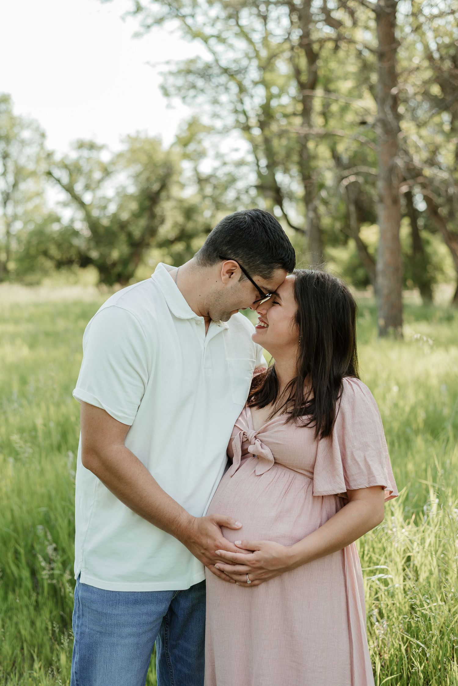 A couple shares an intimate moment in a sunlit meadow while celebrating their pregnancy.