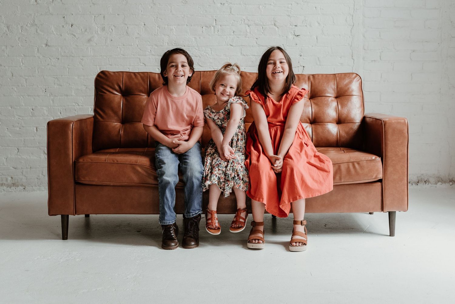 Family members sit closely together on a brown leather sofa in a bright studio.