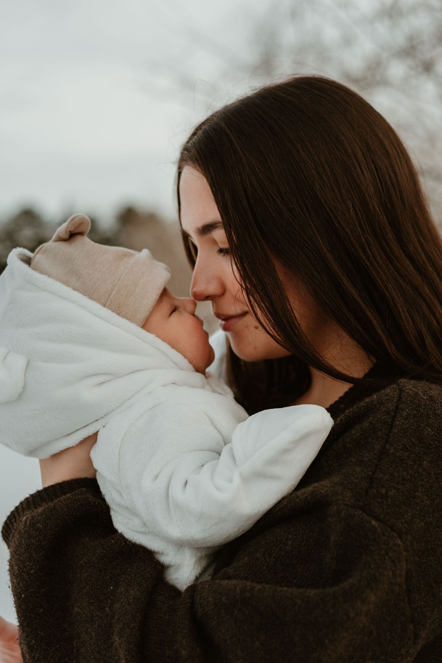 Intimate moment between parent and baby wrapped in white blankets during winter photoshoot.