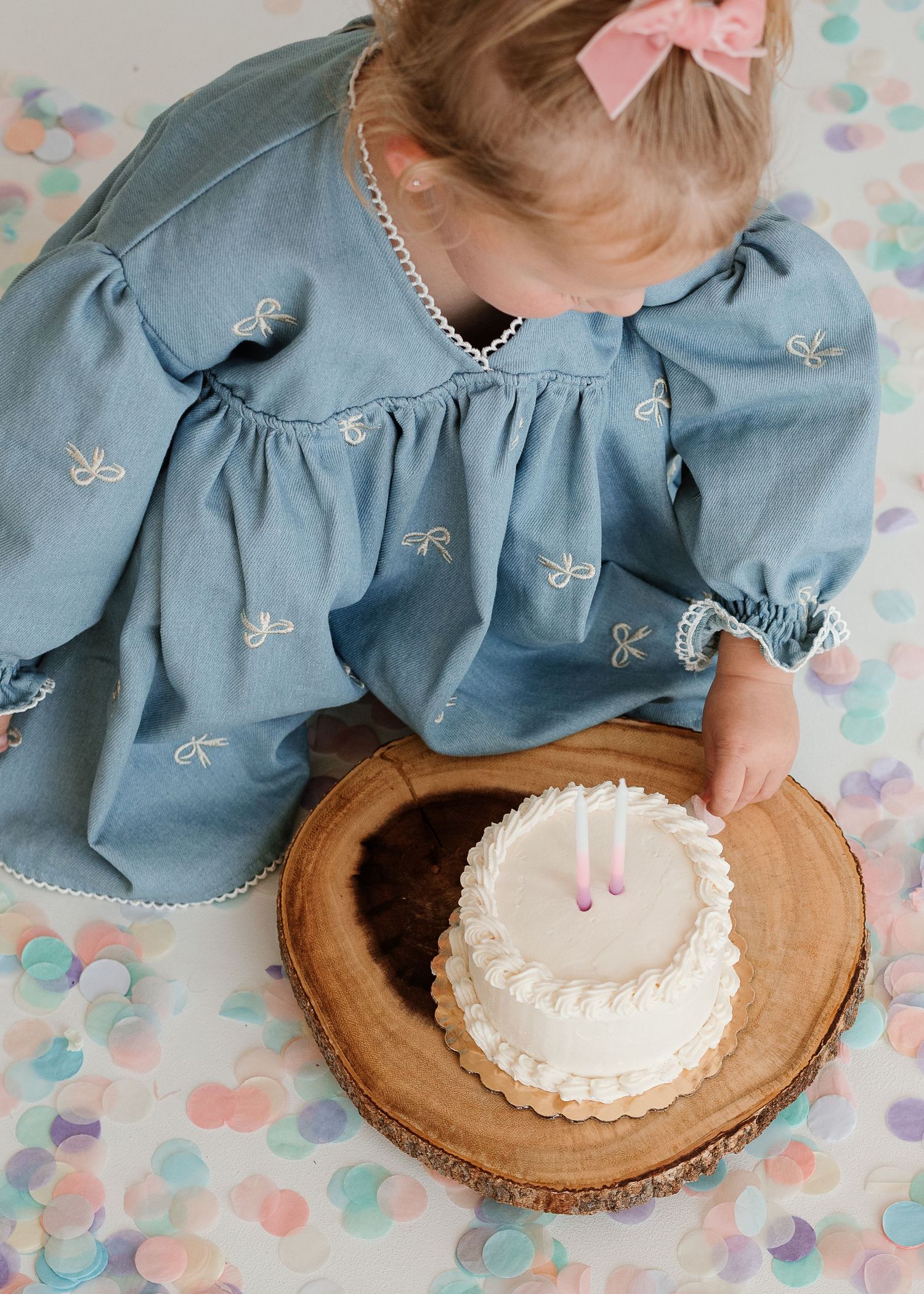 A series of four images showing someone in a blue dress smashing and enjoying a small white frosted cake on a wooden board.
