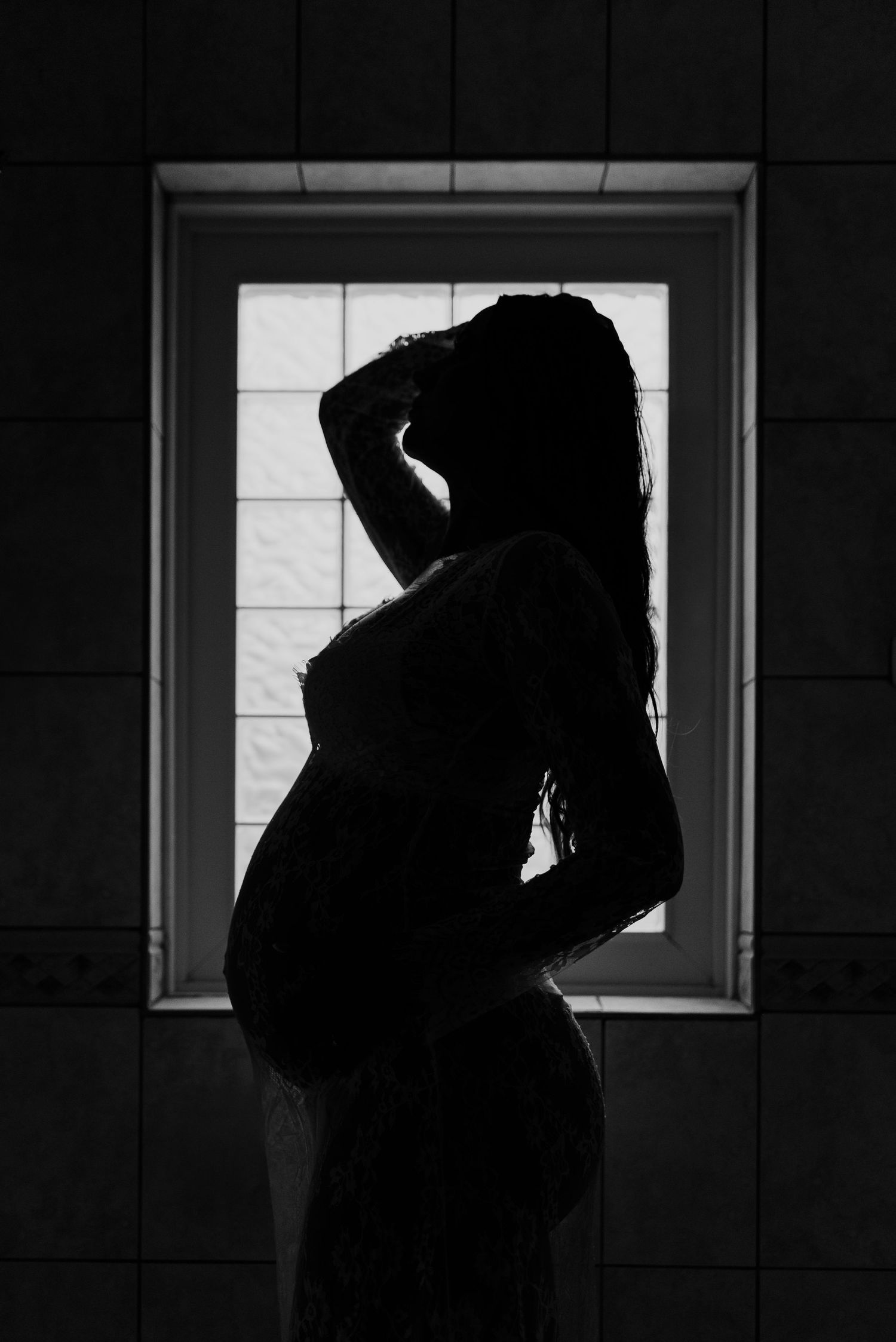 A dramatic black and white silhouette of a pregnant figure standing in front of a window.
