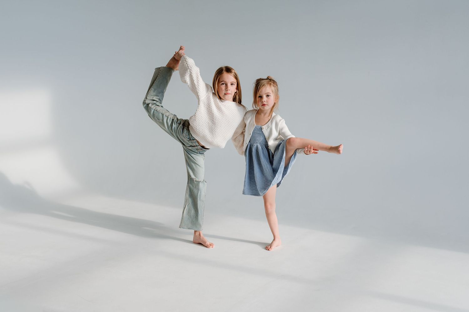 Two people in light colored clothing dance gracefully together against a white background in an artistic photoshoot.