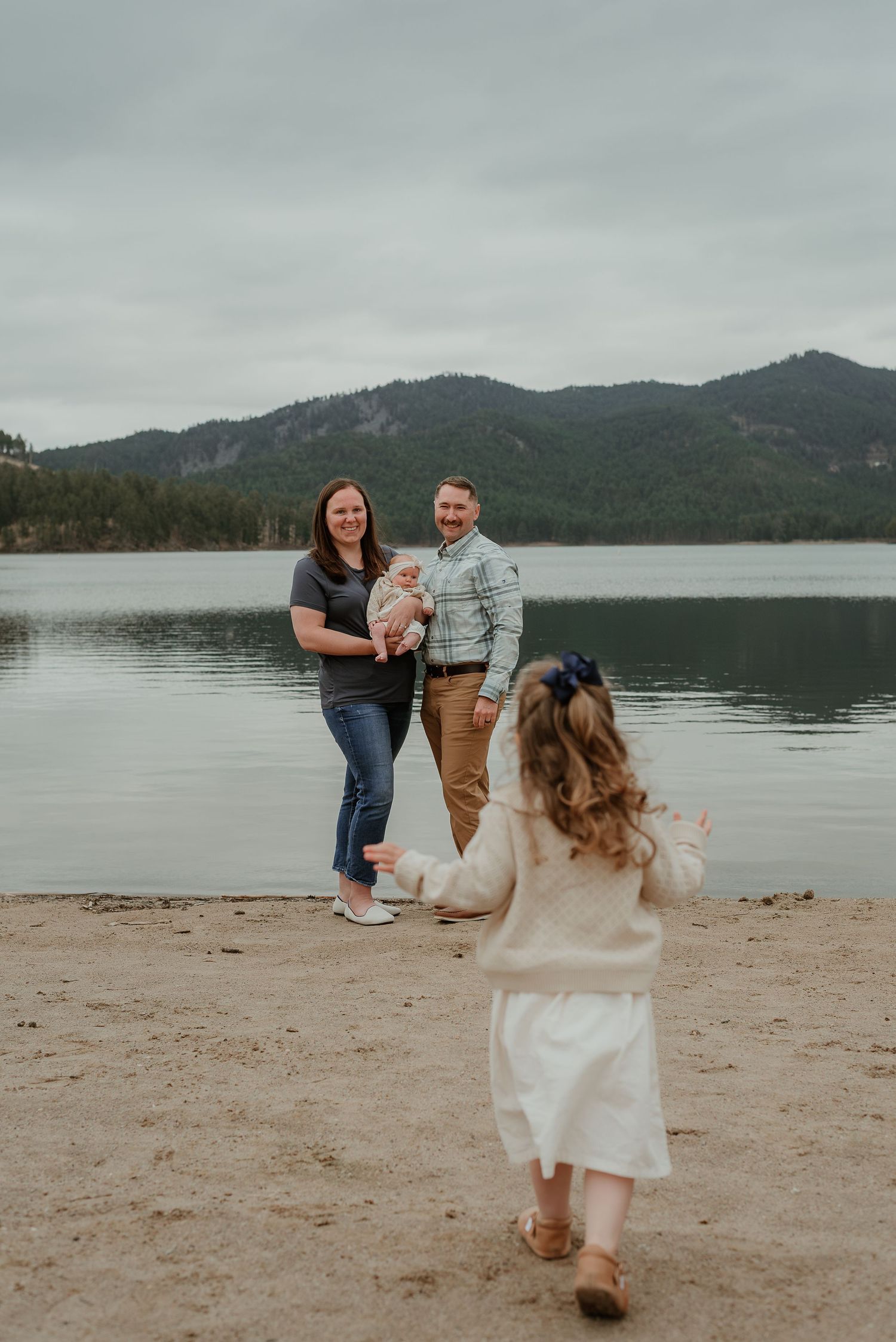 A family enjoys a day at the lake with mountains and evergreen trees in the background.