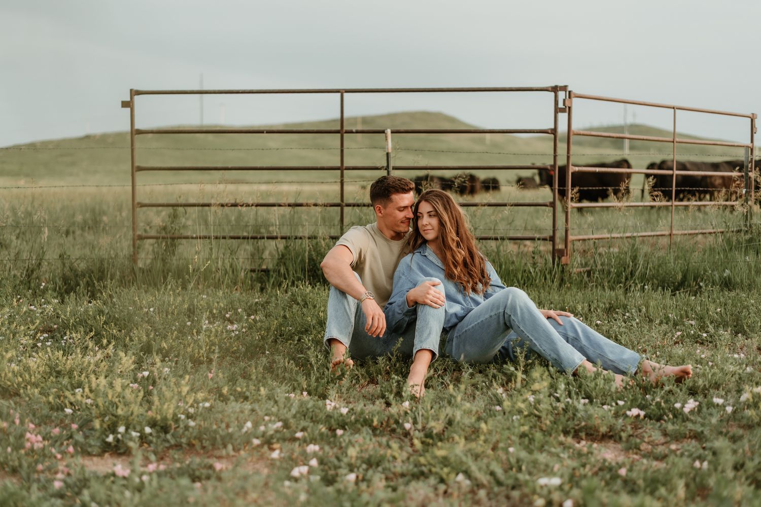 Romantic couple sitting together in a rustic field with metal fencing.