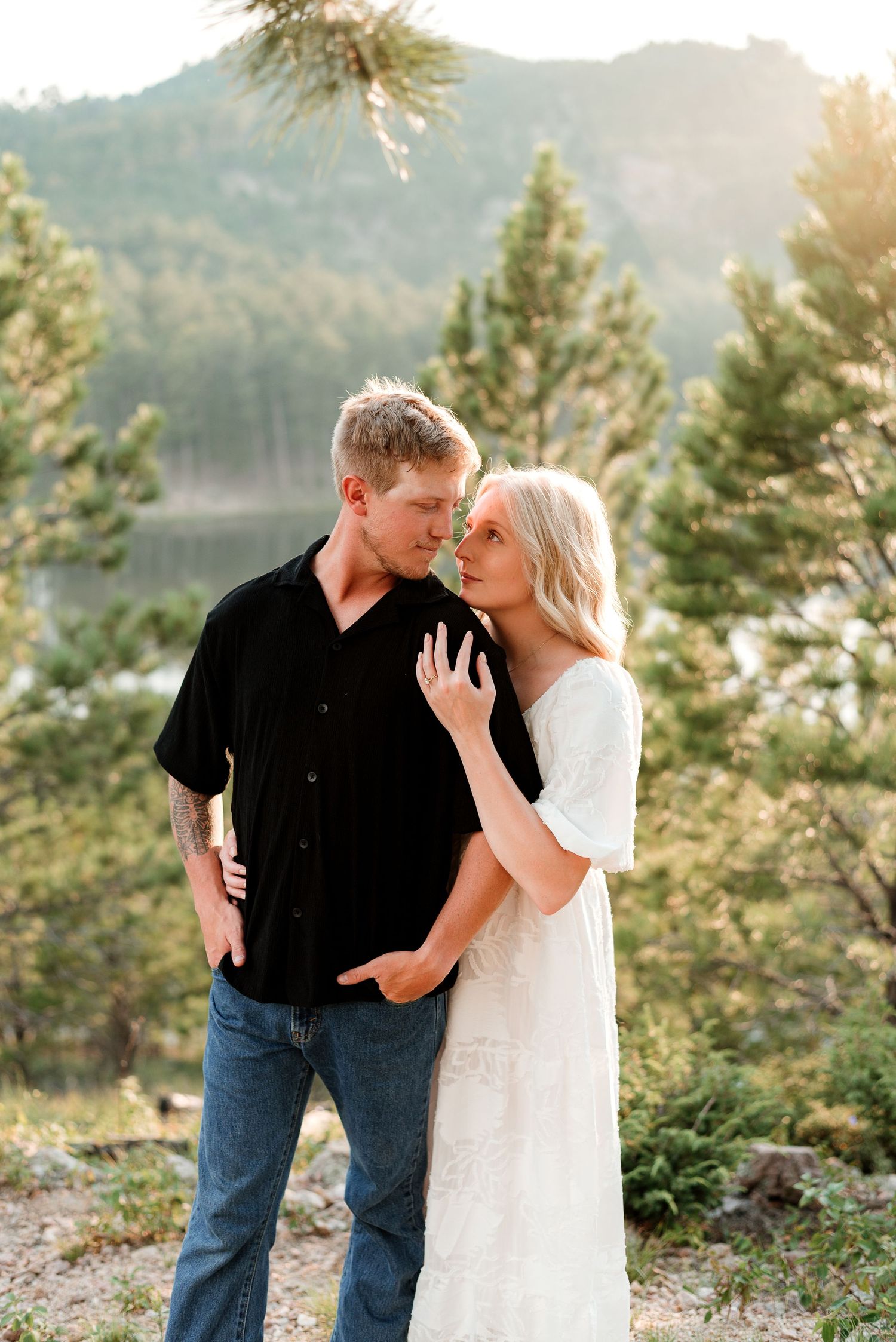 Couple in contrasting black and white outfits share a tender moment in a mountain forest setting.