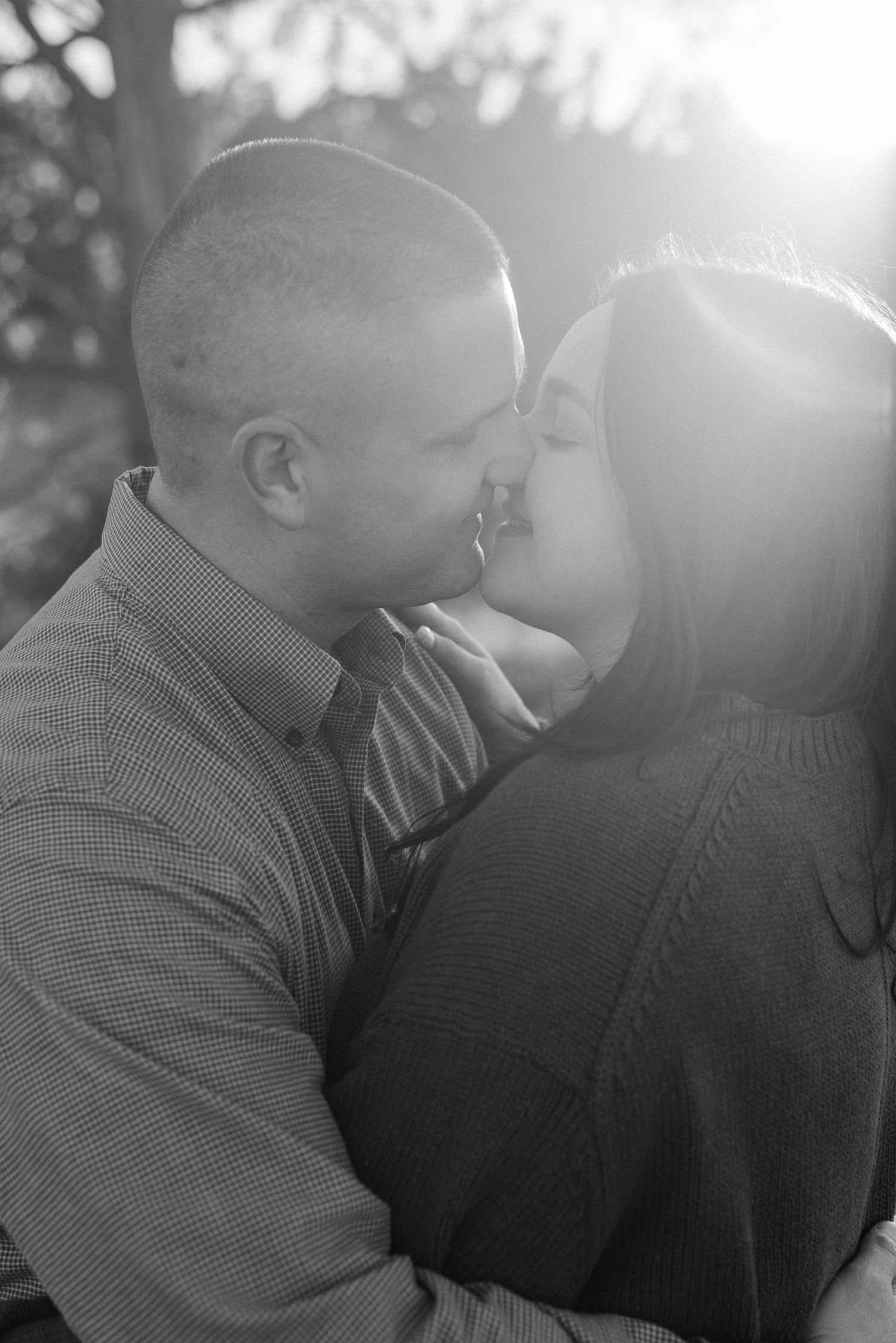 Black and white portrait of couple sharing intimate moment in sunlit outdoor setting.