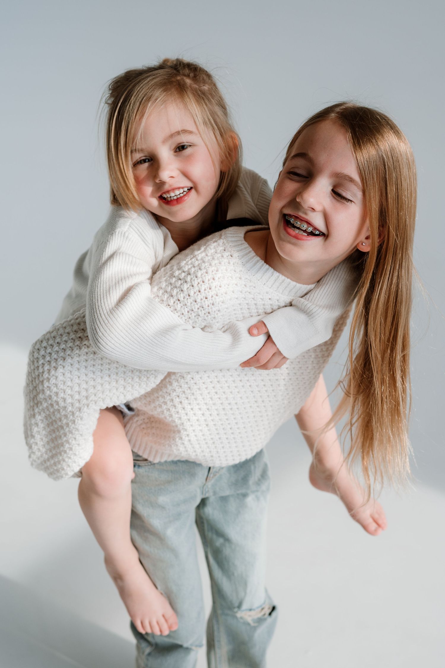 A playful sequence of photos showing joyful movement and dancing in white sweaters and light denim against a gray backdrop.