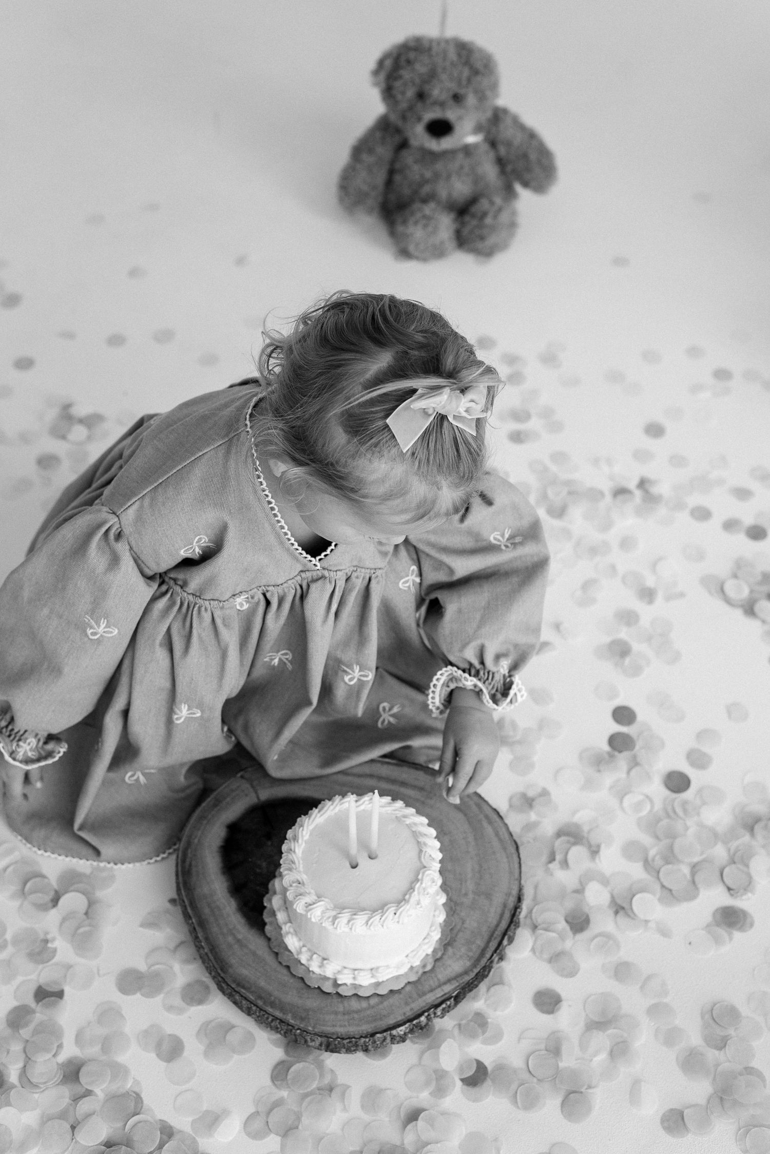 Black and white photos showing a smash cake scene with confetti and a teddy bear watching.