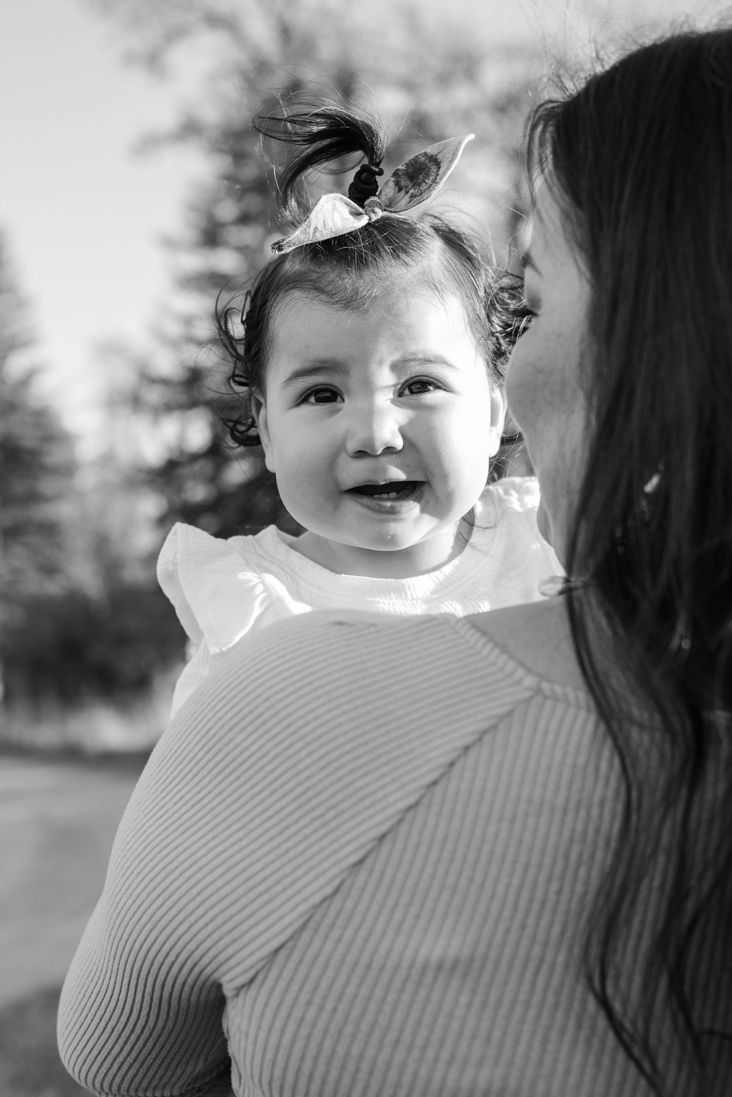Black and white portrait of a smiling baby wearing a bow in their hair.