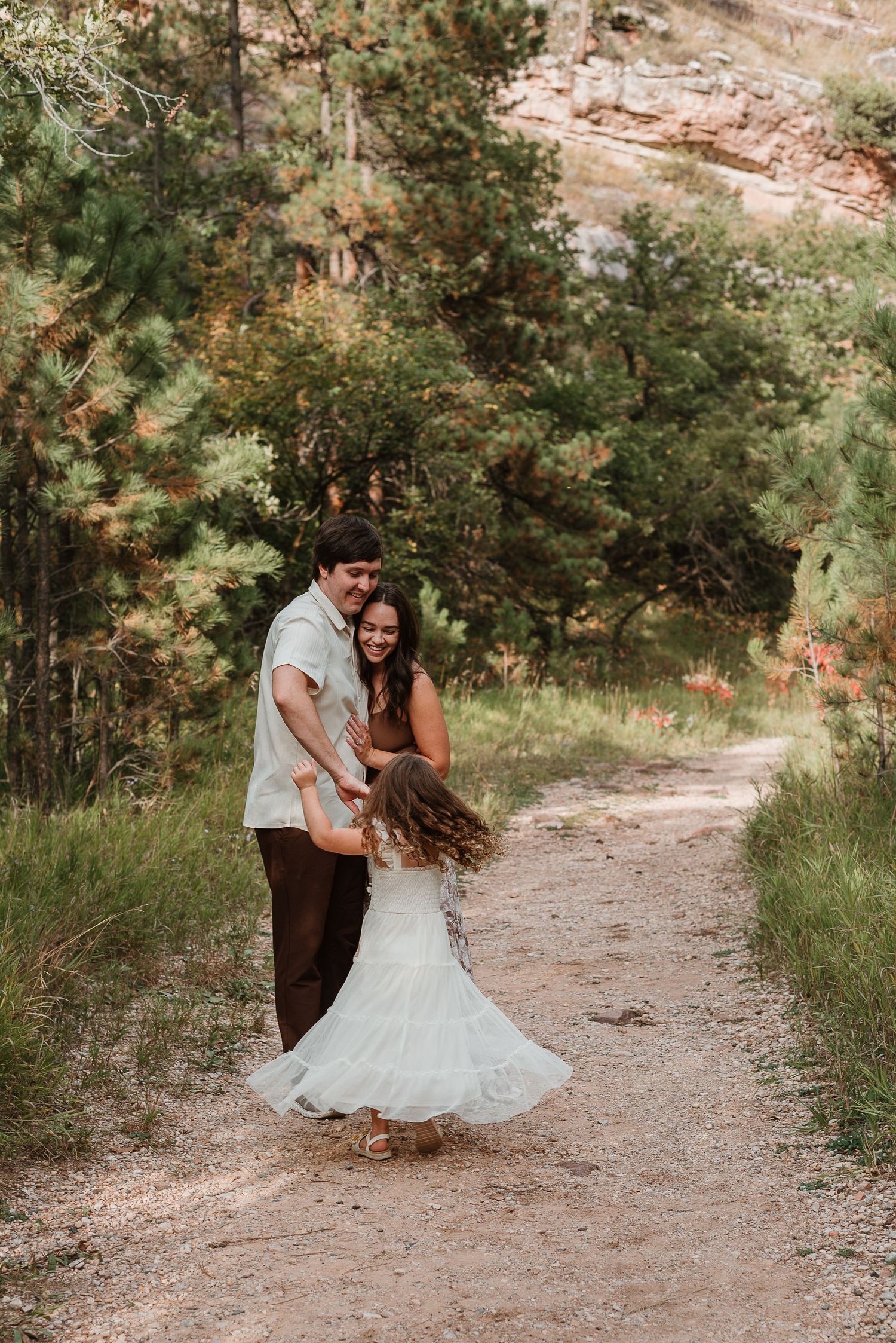 A couple shares a romantic moment together on a winding dirt path surrounded by lush greenery and red rock formations.