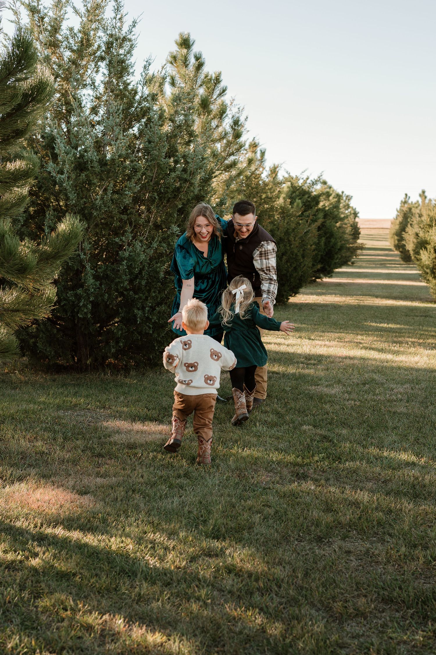People running and playing together on a grassy hill during golden hour with evergreen trees in the background.