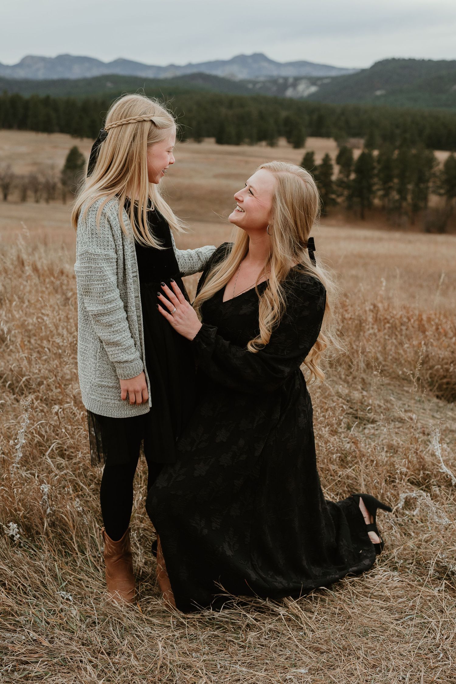 Candid family moment captured in a golden field with mountains and forest in the background.