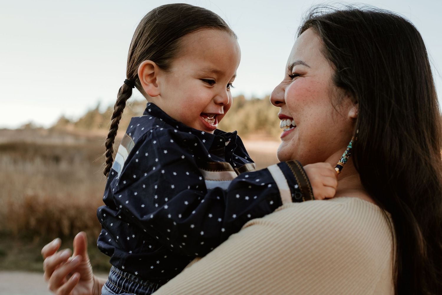 Close-up portrait of shared laughter and joy between parent and child outdoors.