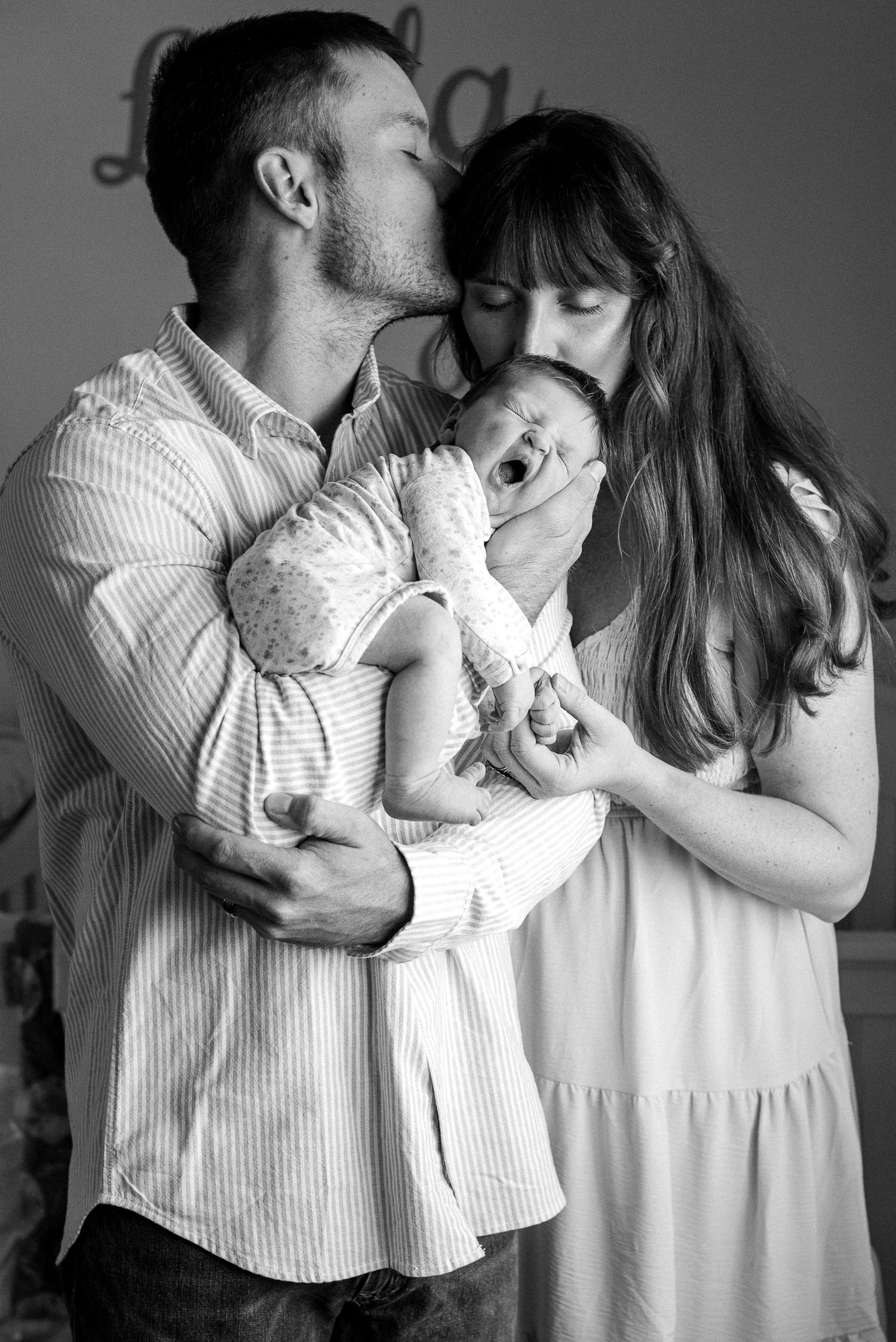 A series of black and white photos showing tender family moments with a baby in white clothing.