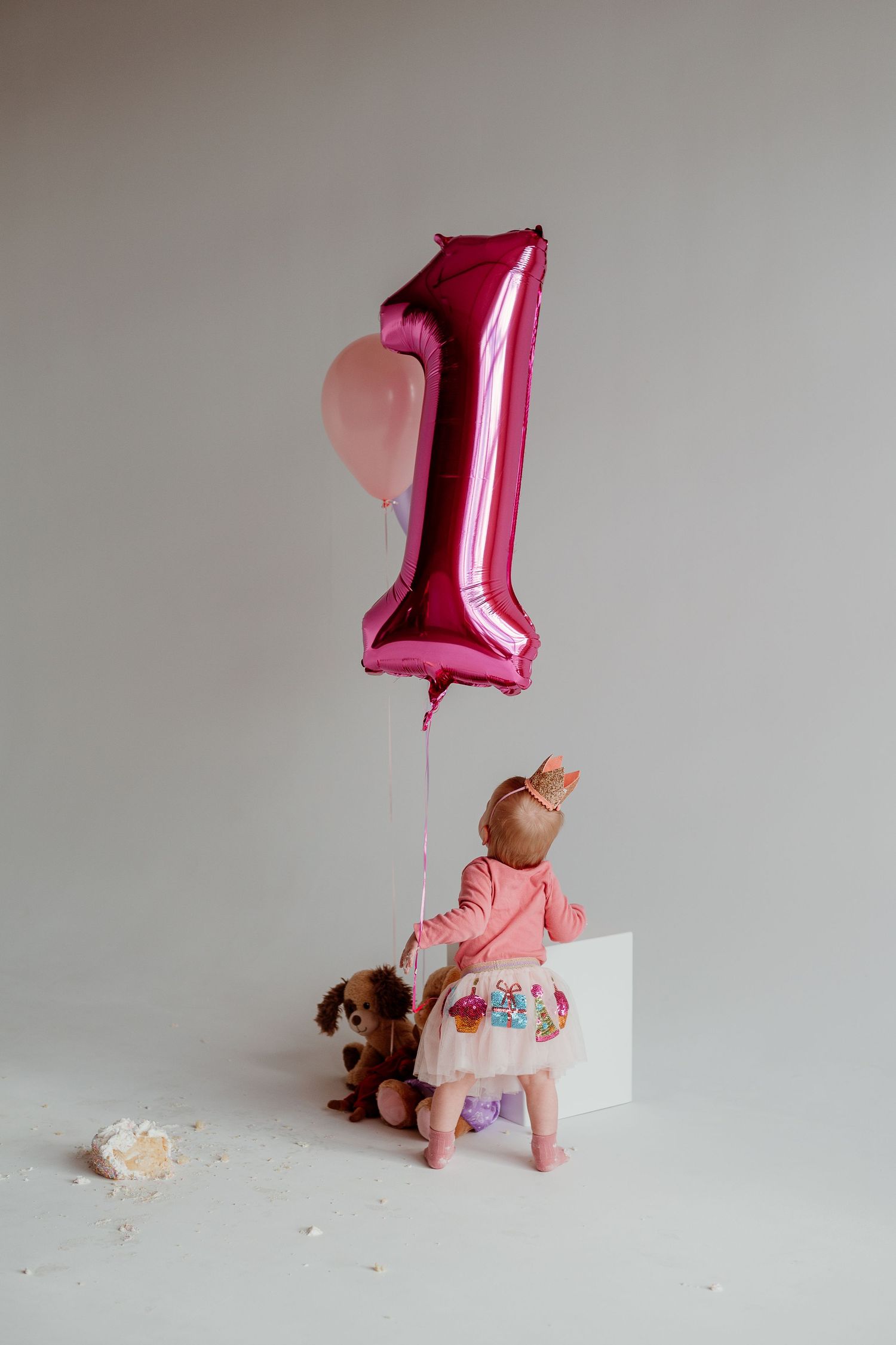 Pink number one balloon and stuffed toys arranged in progressive studio shots against gray background.