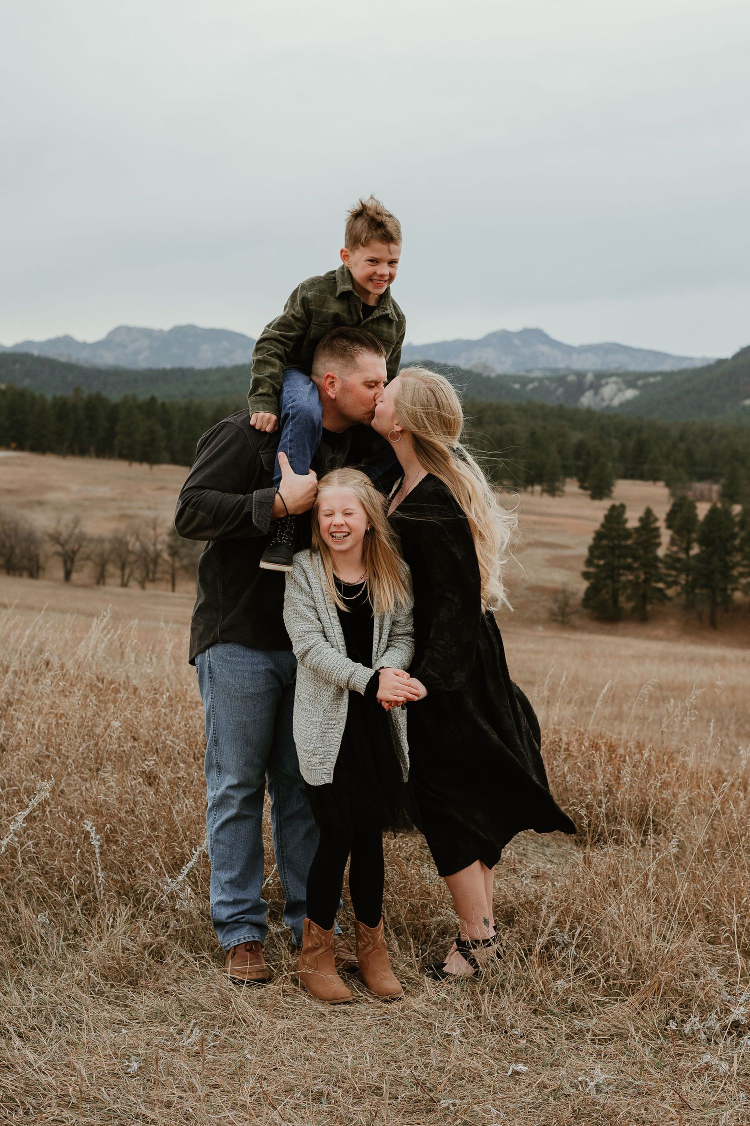 Joyful outdoor family portraits in a rustic field with mountain landscape backdrop.