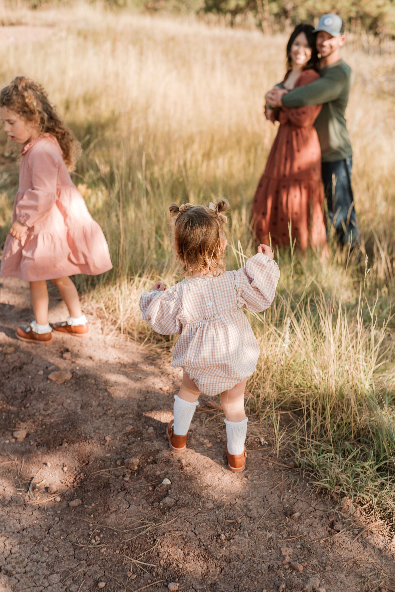 Family enjoying a sunny day outdoors in a golden field with children playing in rustic dresses and casual attire.
