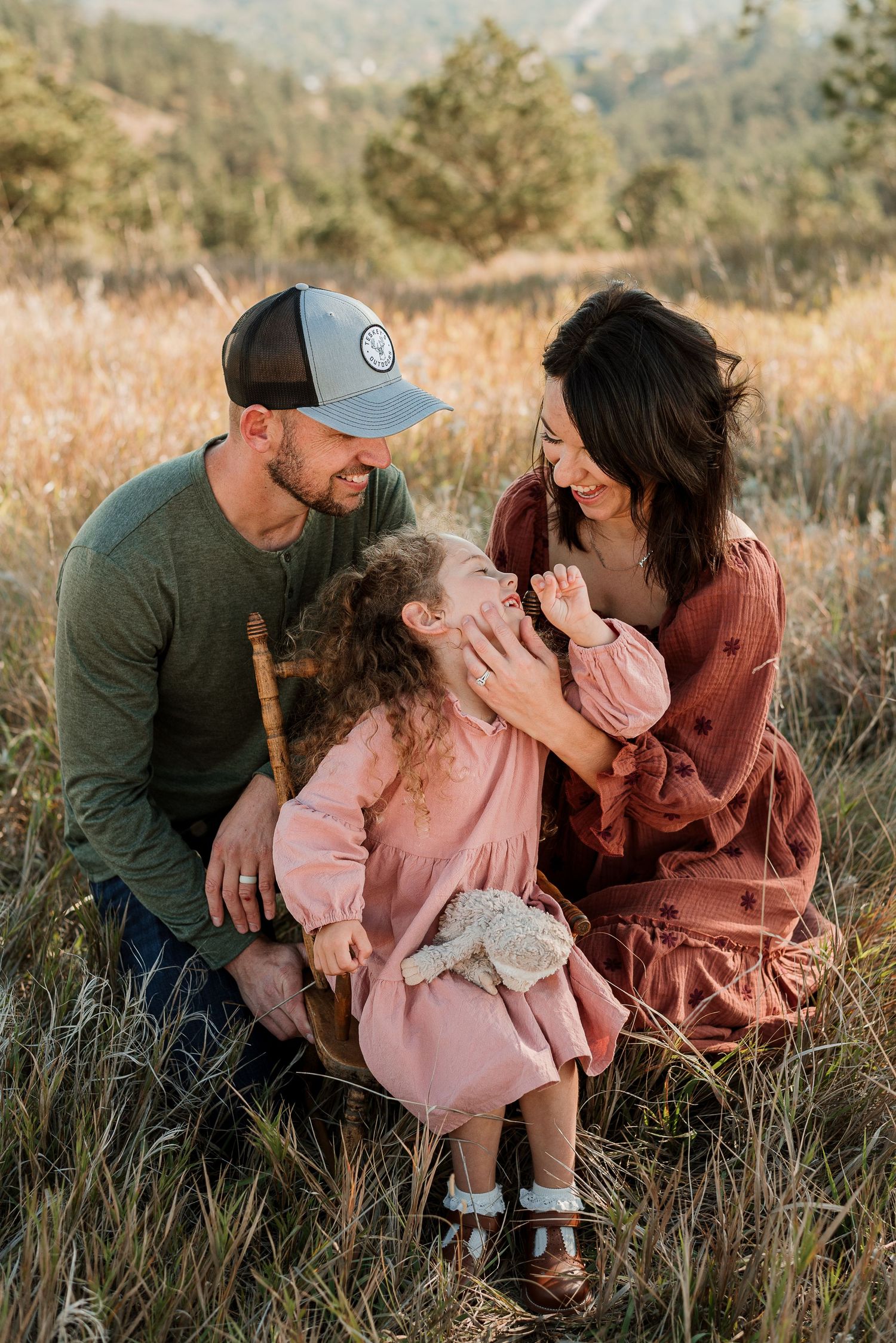 A family sits together in a grassy field during golden hour, sharing tender moments and laughter.