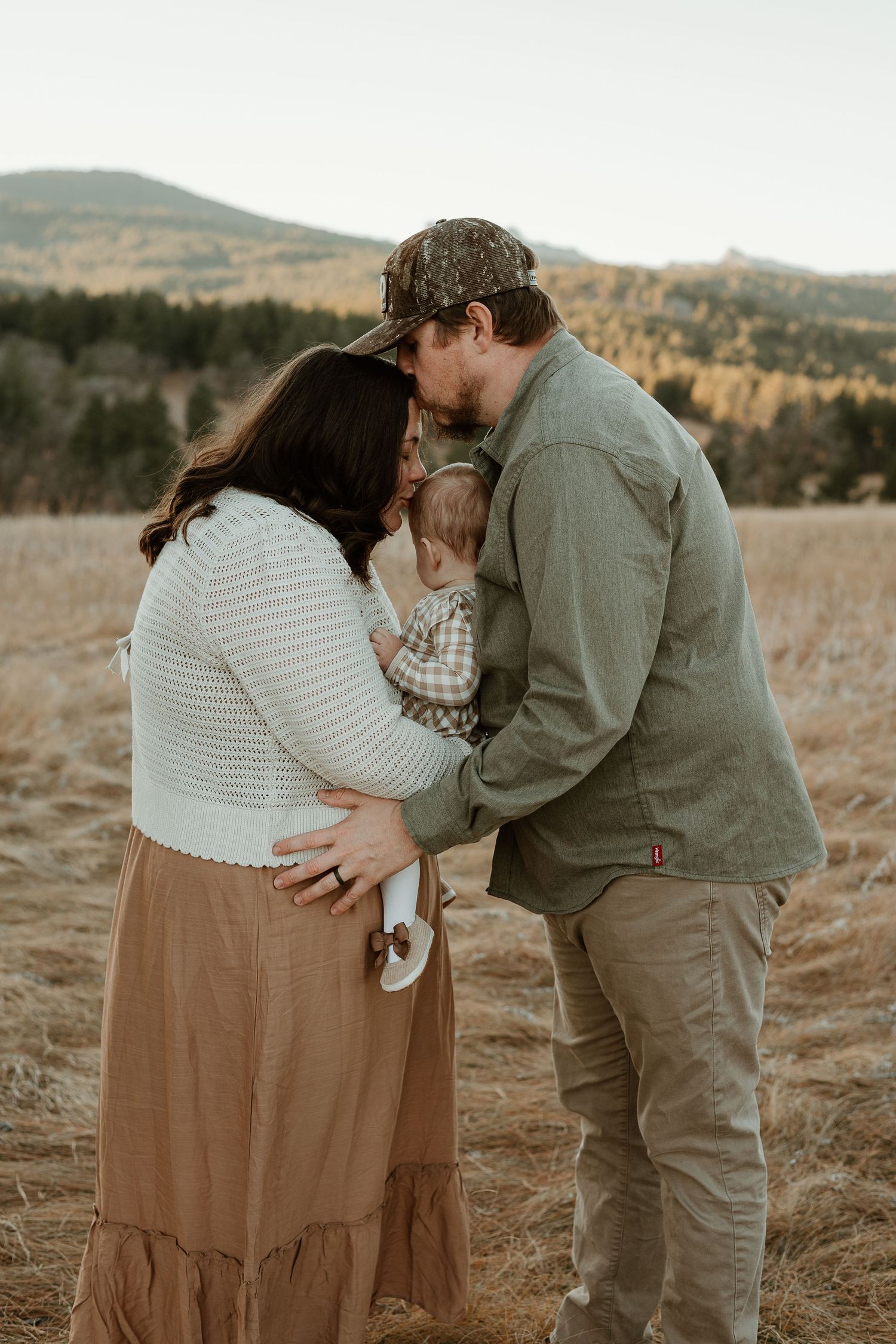 A romantic couple embracing in a rustic outdoor setting with mountains visible in the distance.