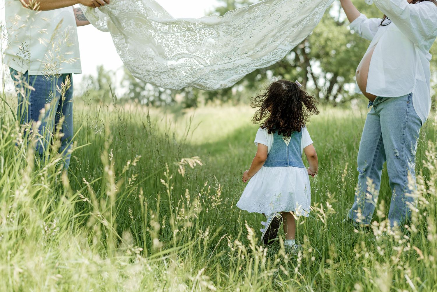 A child plays under a white fabric canopy in a grassy meadow.