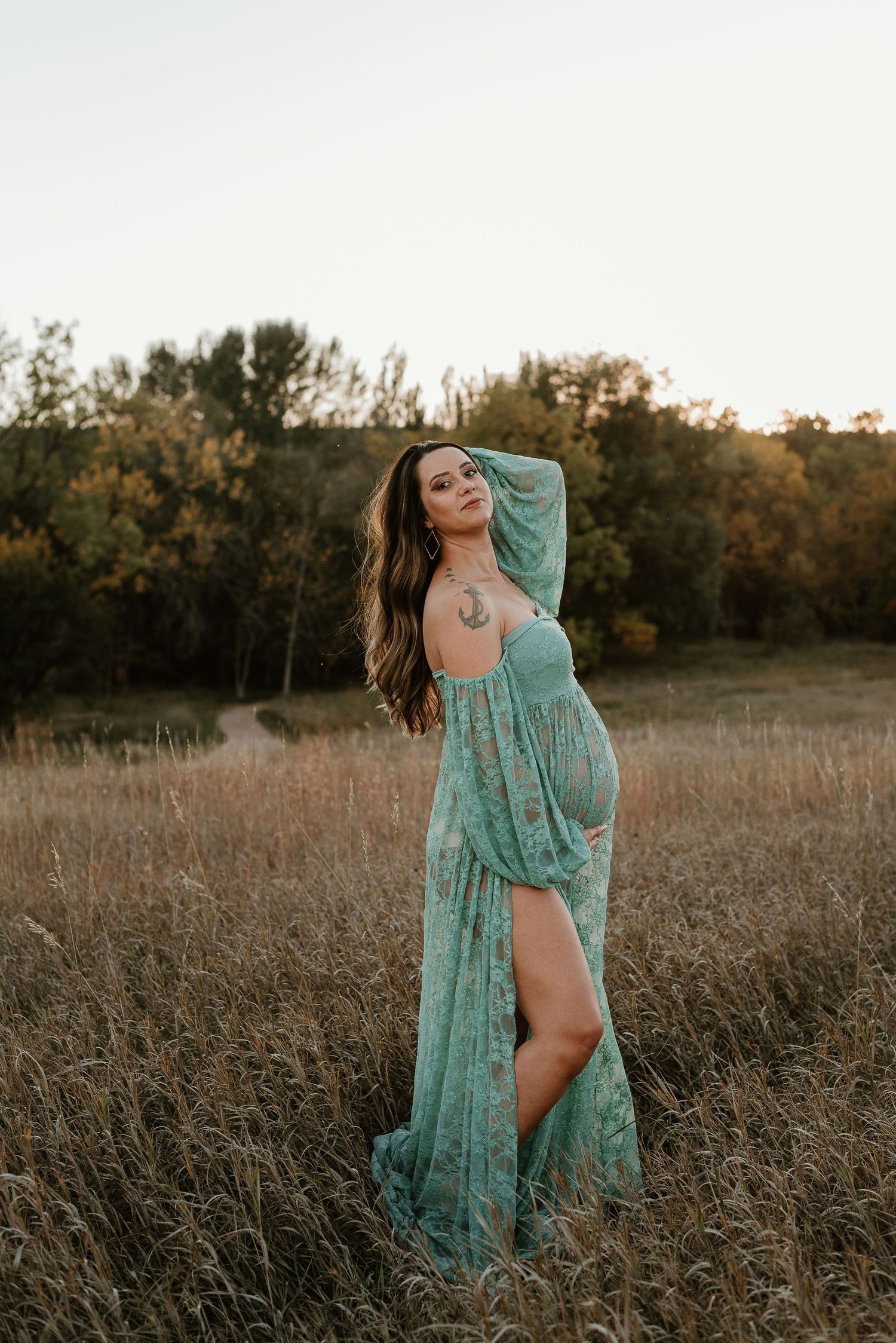 A woman in a turquoise lace dress poses gracefully in a golden autumn field during sunset.