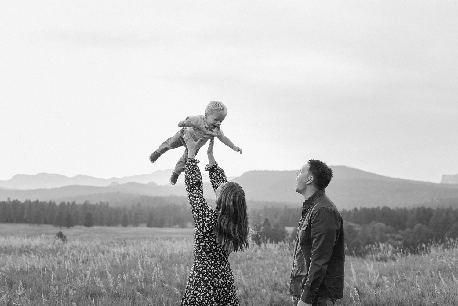 A couple dances together in a field at sunset with mountains visible in the background.