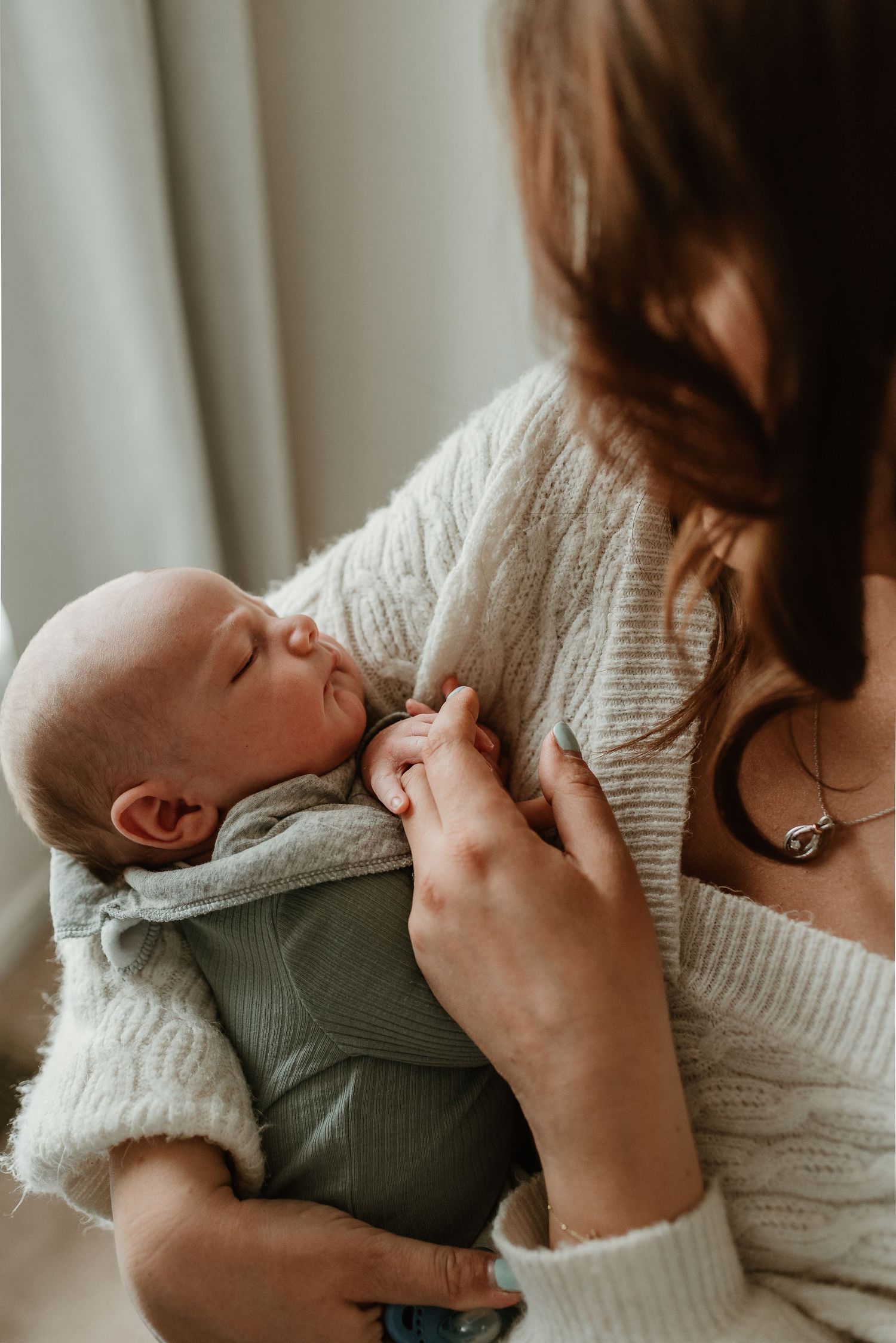 Intimate sequence of parent in cream sweater holding and bonding with baby in sage green outfit.
