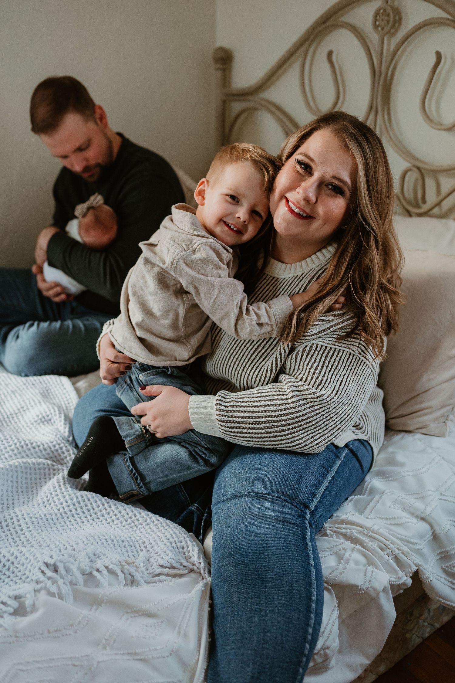 A cozy family moment on a bed with white linens and an ornate metal headboard.