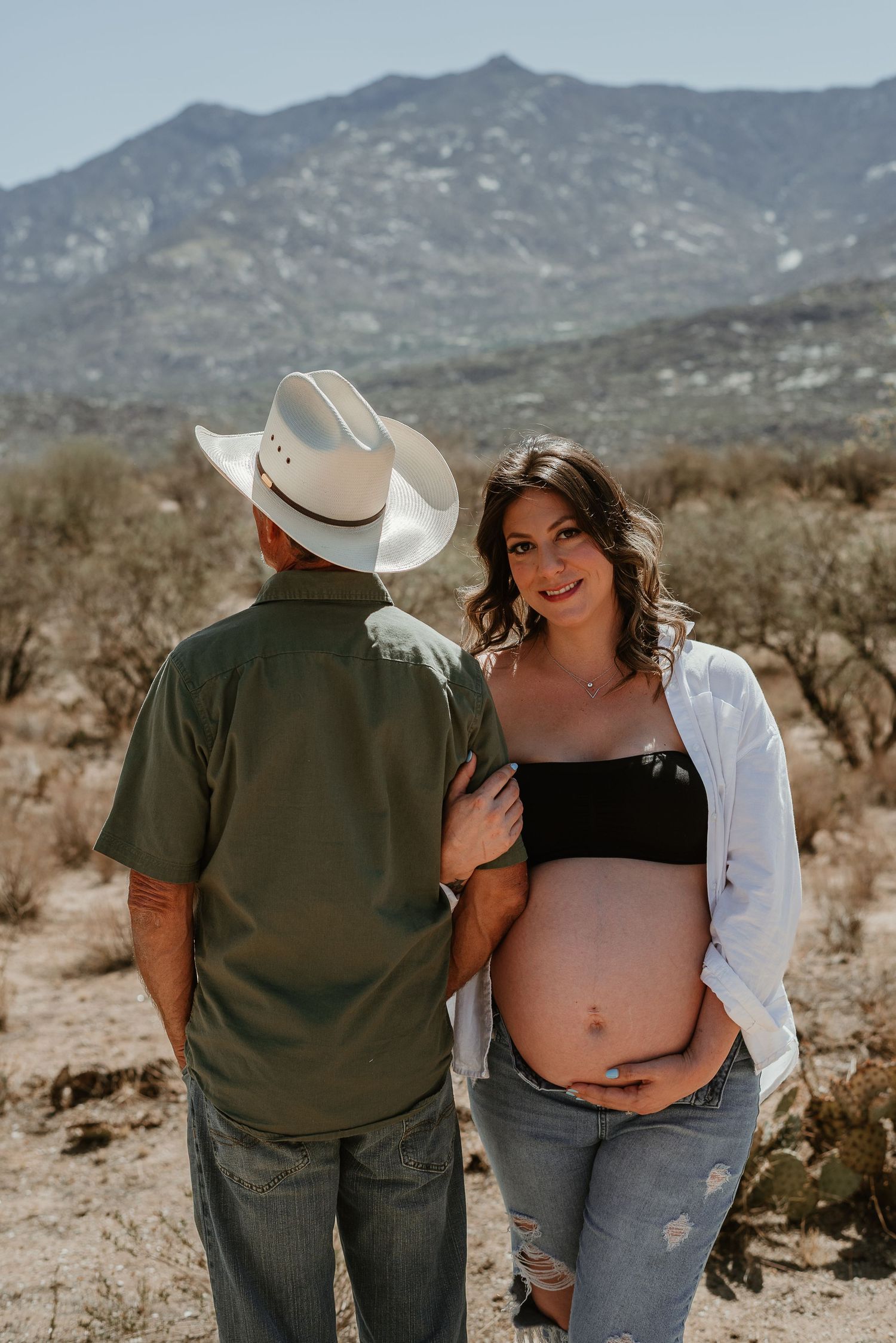 Couple posing in casual attire against rugged desert mountain landscape.