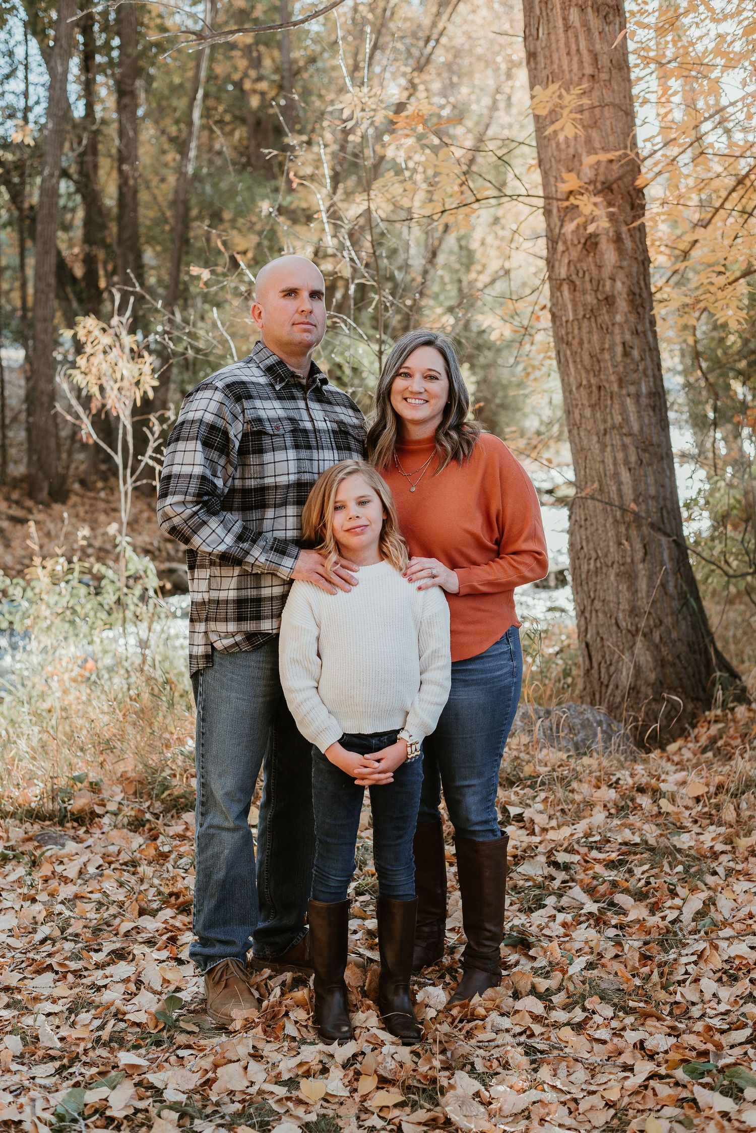 Family portrait in autumn forest with fallen leaves and tall trees.
