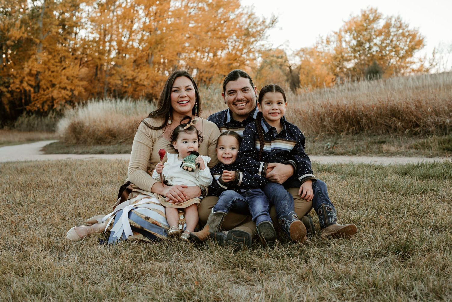 Family relaxing together on grass in autumn field with warm sunset lighting.